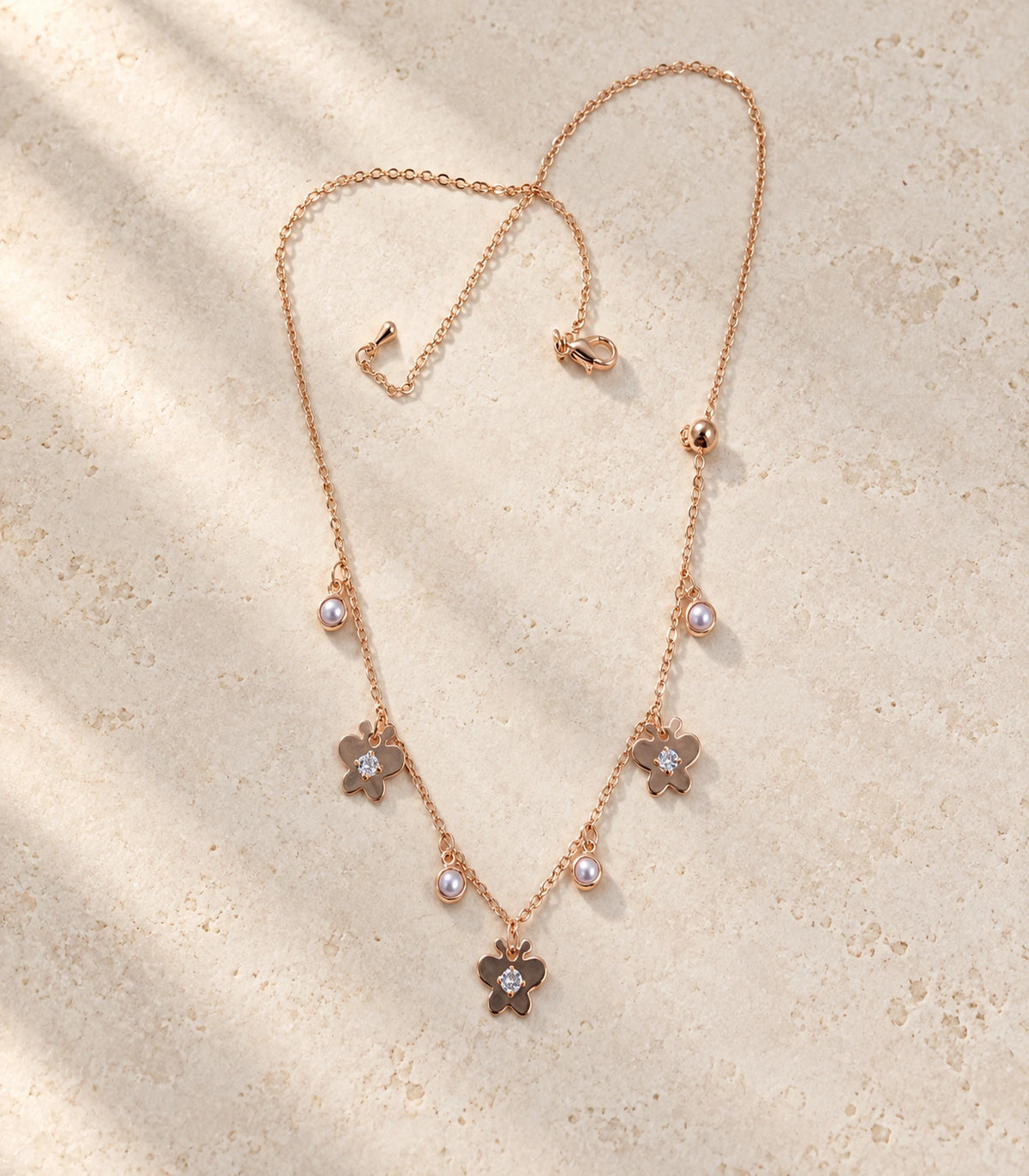 JIMIKI Rose Gold Pearl Effect Butterfly Charm Necklace - complete butterfly necklace in a styled flat lay #color_rose-gold