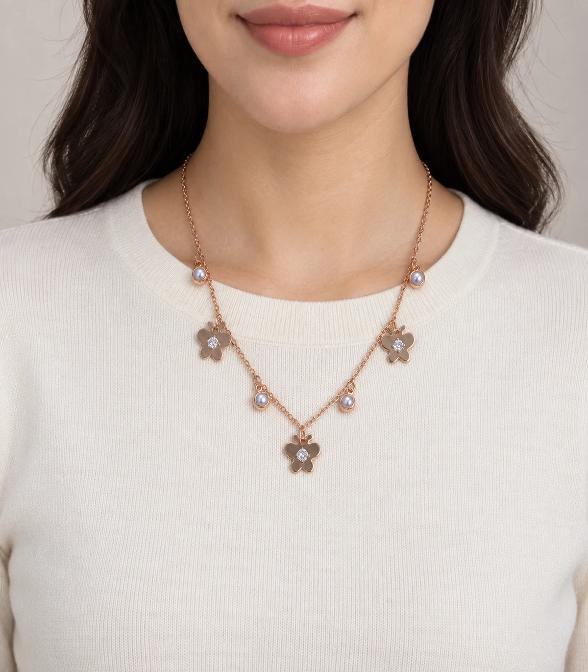 JIMIKI Rose Gold Pearl Effect Butterfly Charm Necklace - butterfly charm necklace worn against an ivory top #color_rose-gold