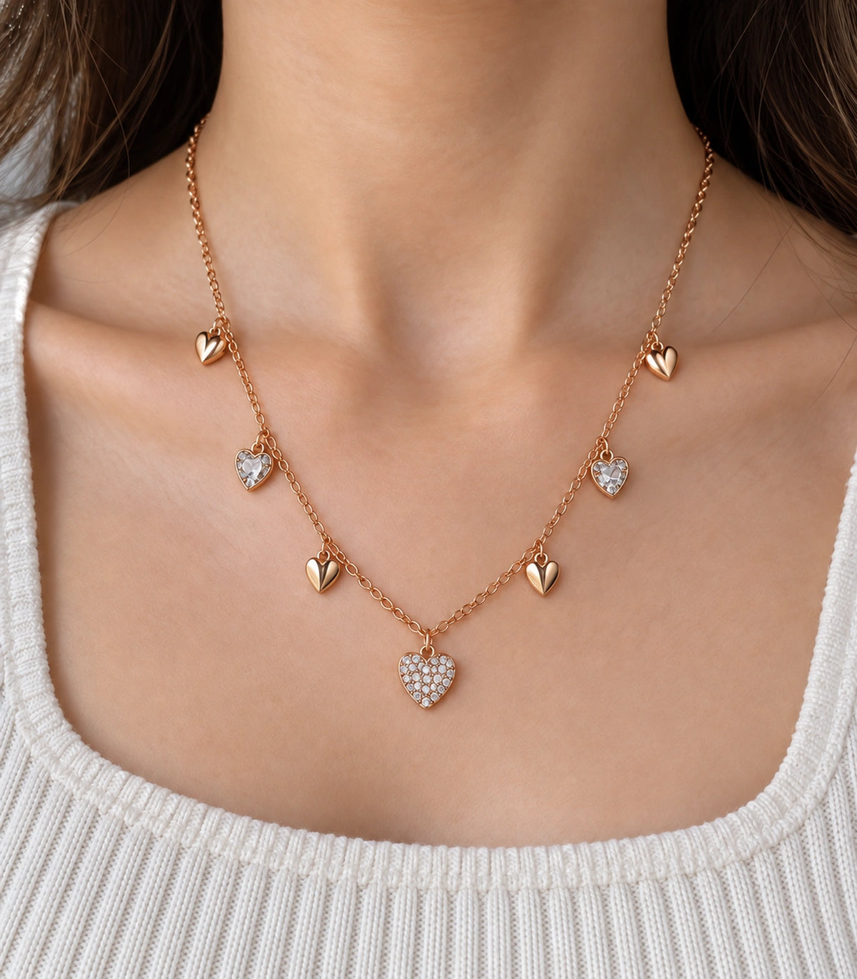 JIMIKI rose gold-tone seven heart charm necklace, close view of creased polished hearts, single-stone side hearts and central pave-style heart #color_rose-gold