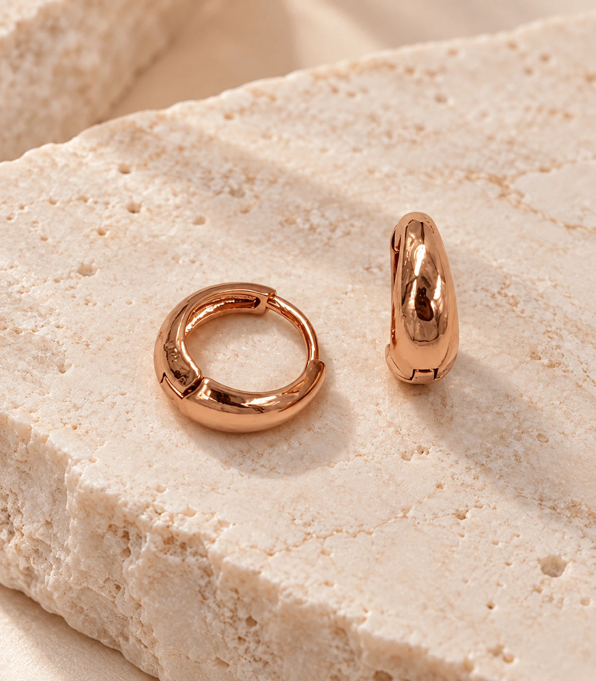 JIMIKI Smooth Tapered Huggie Earrings in Rose Gold Tone — editorial flat lay #color_rose-gold-tone