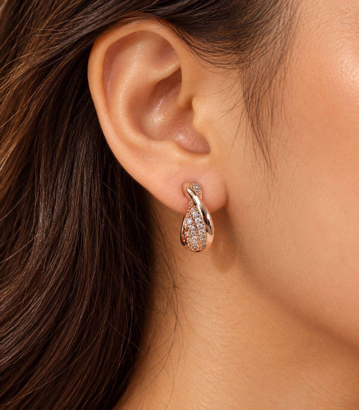 JIMIKI Rose Gold Tone crossover pave huggie hoop earrings, worn in warm editorial lighting #color_rose-gold-tone