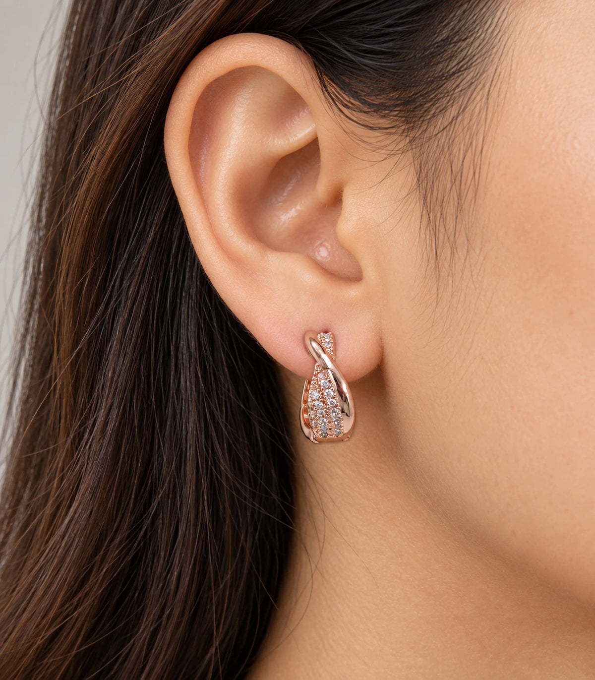JIMIKI Rose Gold Tone crossover pave huggie hoop earrings, worn on the ear #color_rose-gold-tone