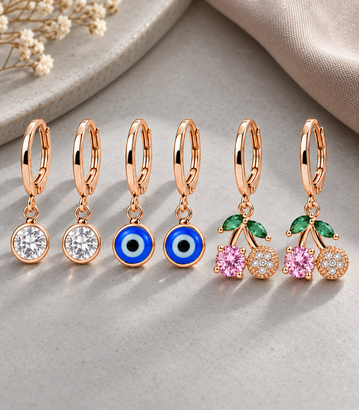 Complete three-pair rose gold tone charm hoop earring set arranged on a grey surface
