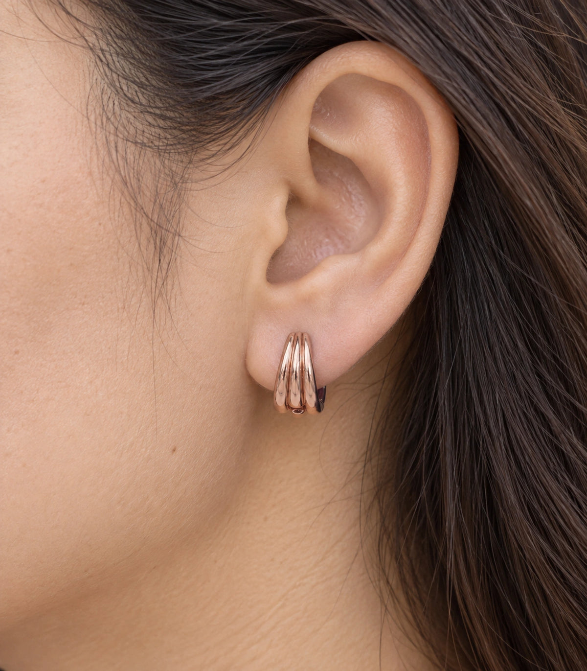 JIMIKI Triple-Ridge Huggie Hoop Earrings in Rose Gold Tone - closeup #color_rose-gold-tone