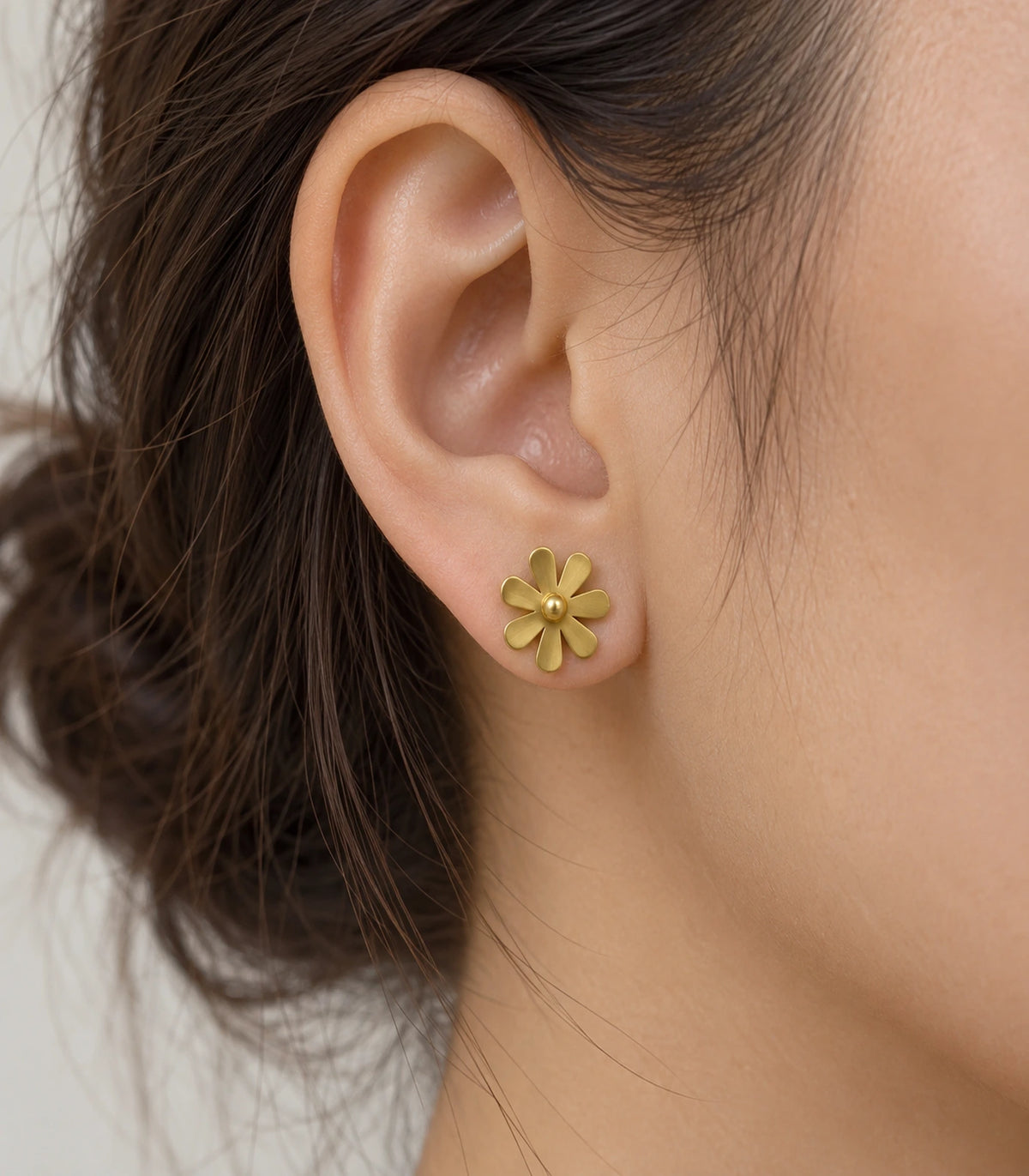 JIMIKI Satin Gold Seven-Petal Daisy Stud Earrings, single stud worn in warm light with hair tucked back #color_satin gold