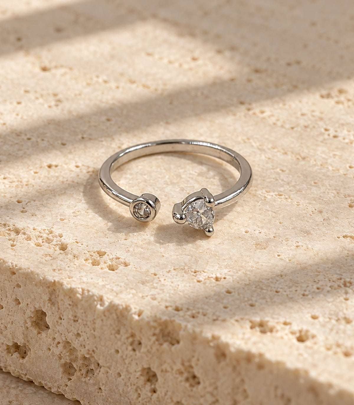 Complete silver-tone asymmetric two-crystal-style open ring on a cream stone surface