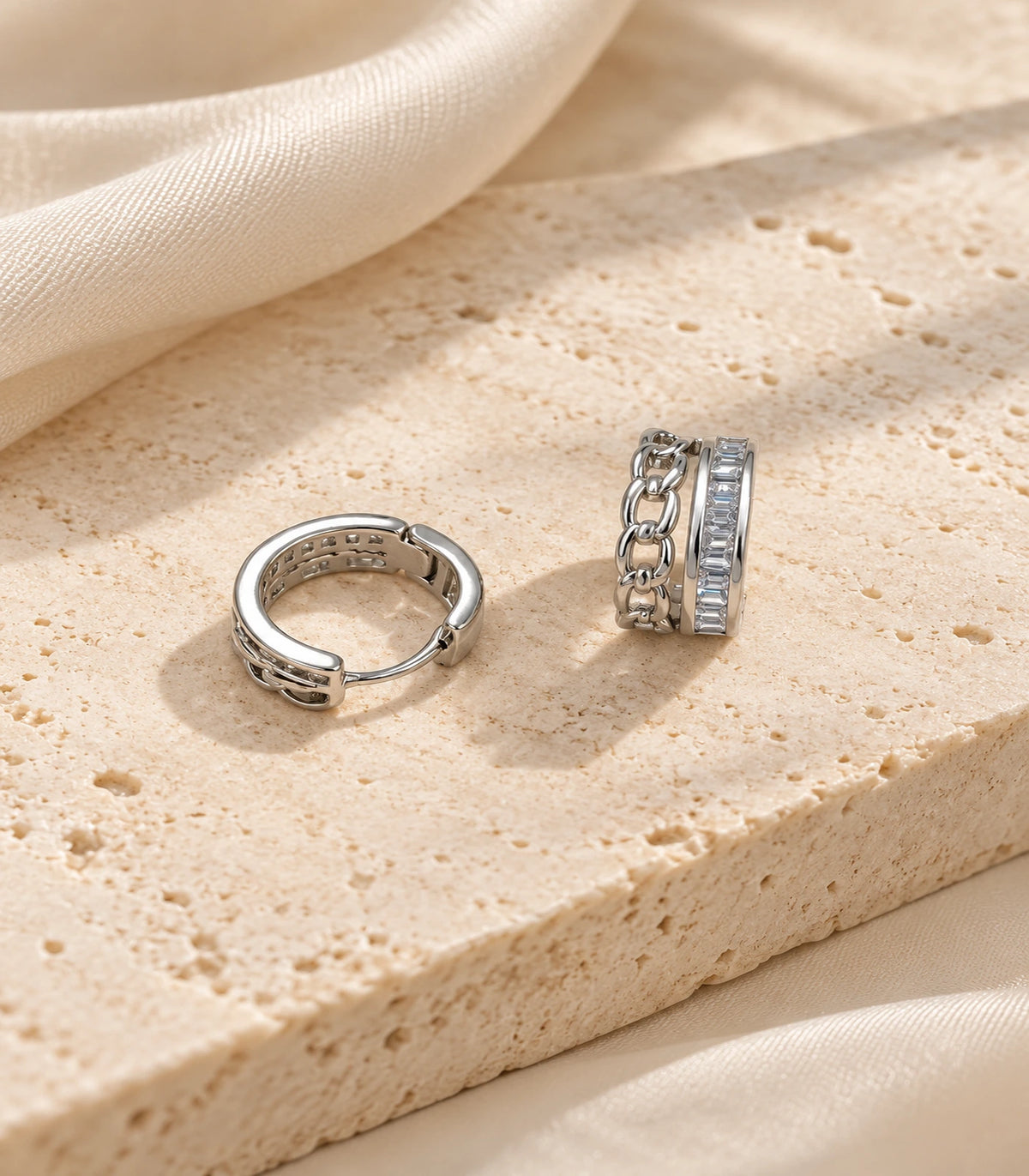 JIMIKI silver baguette chain double row huggie earrings, pair styled on textured stone #color_silver