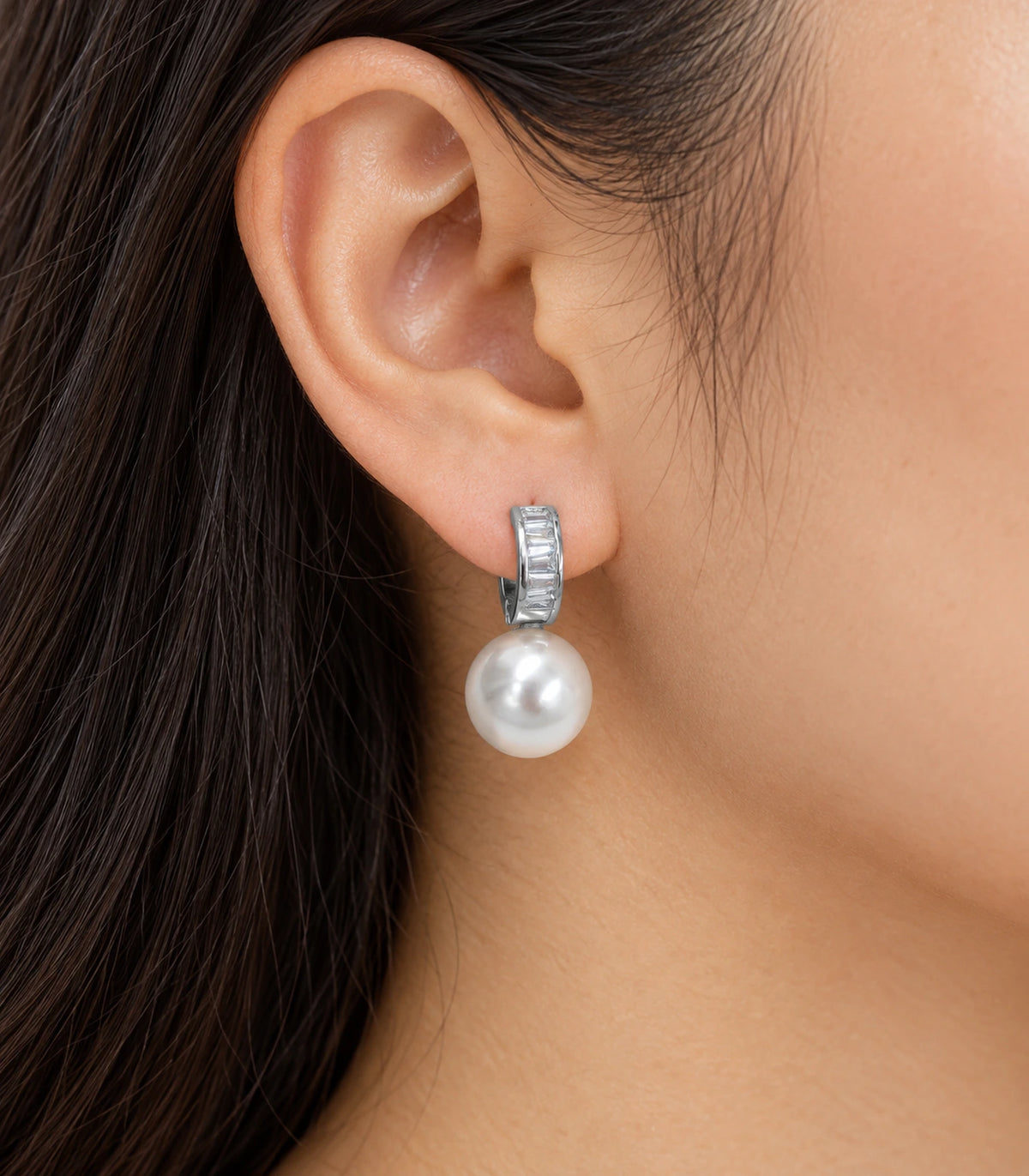 Silver baguette huggie earring with a white pearl-style drop worn on an ear