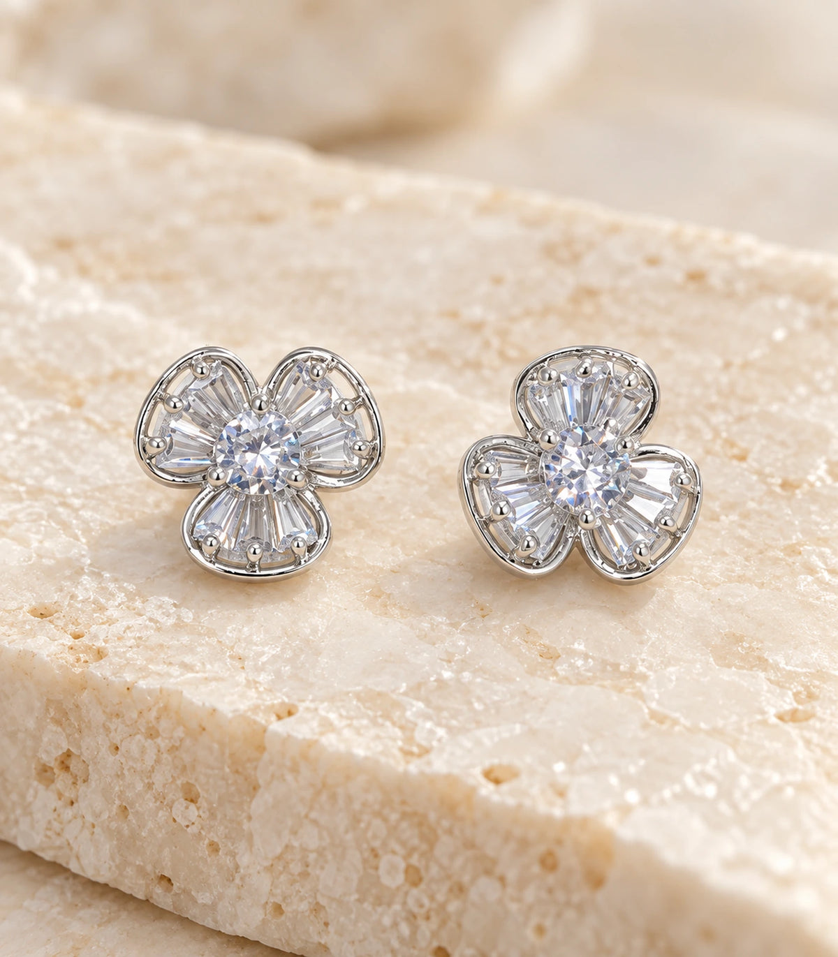 Pair of silver-tone three-petal studs showing clear fan-arranged stones on beige stone