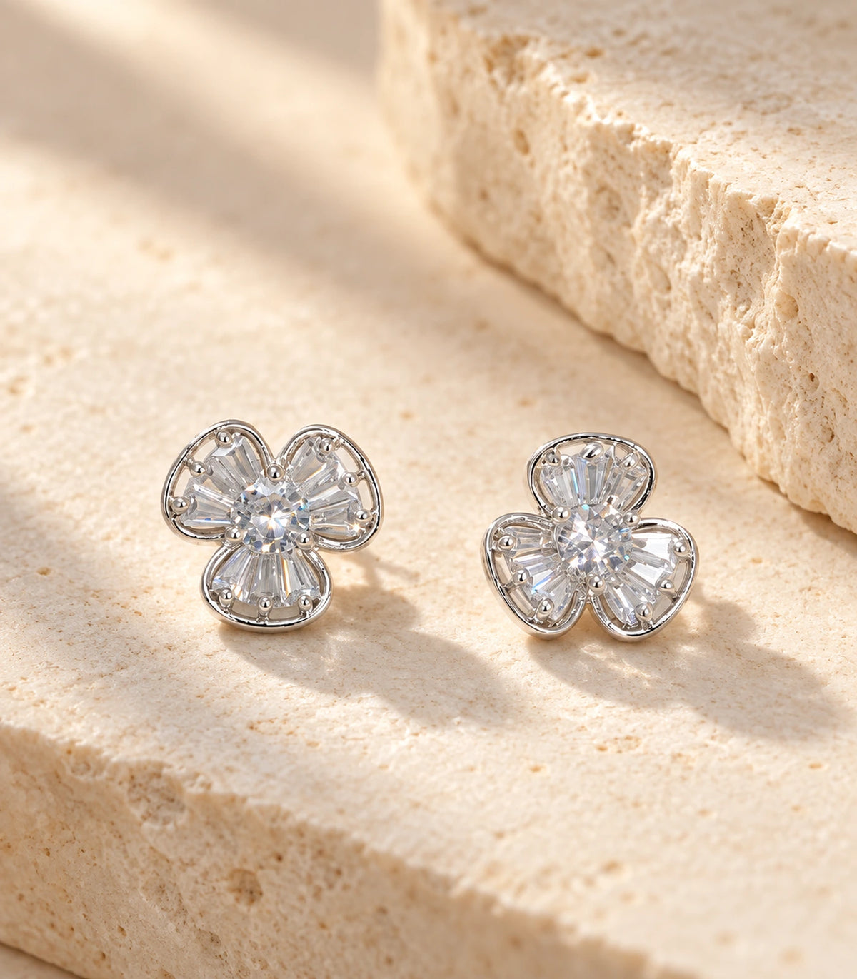 Matching silver-tone three-petal flower stud earrings styled on beige stone