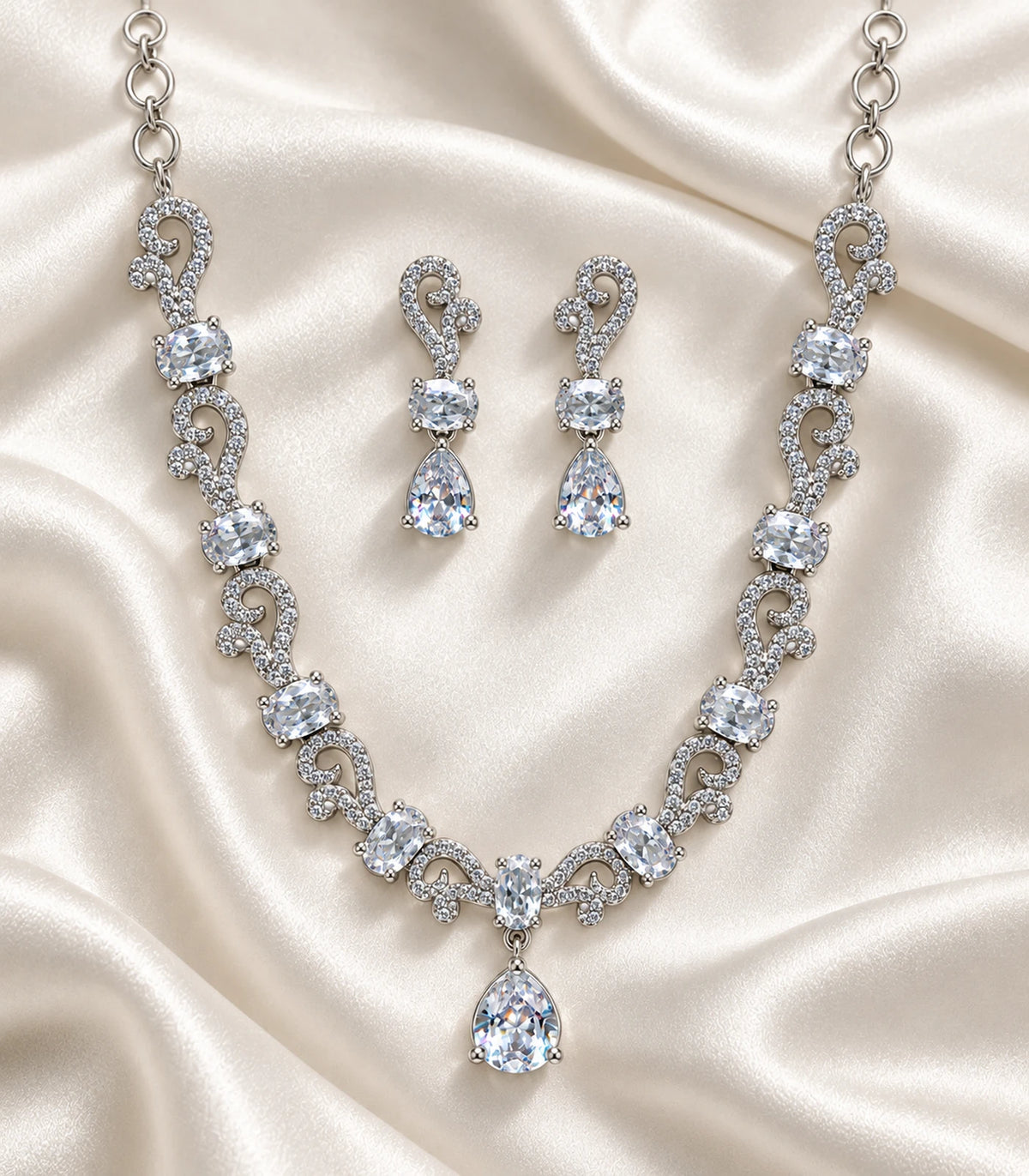 Silver clear paisley necklace and matching drop earrings arranged on ivory fabric