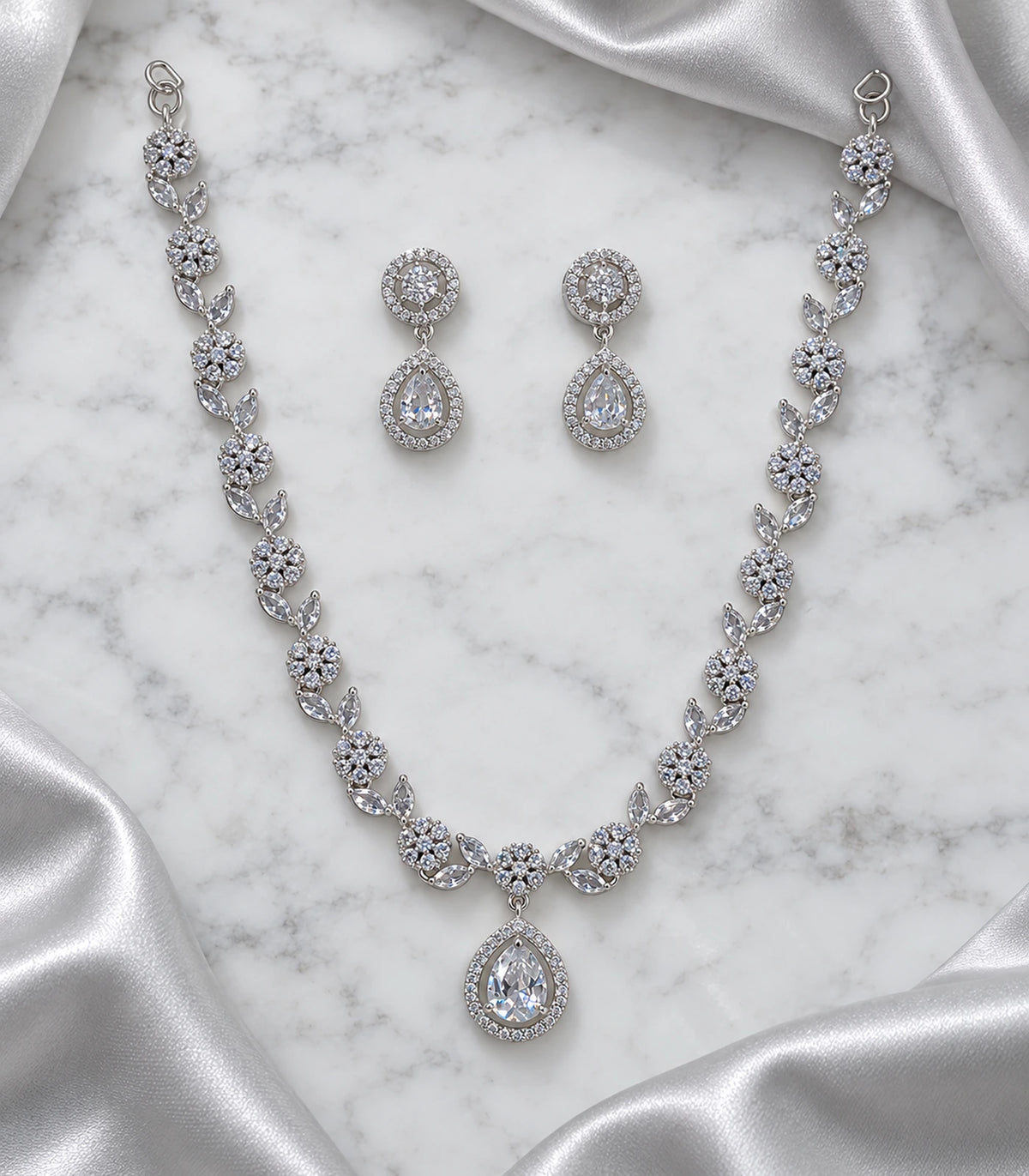 Silver clear crystal necklace and matching earring pair arranged on marble with silver fabric