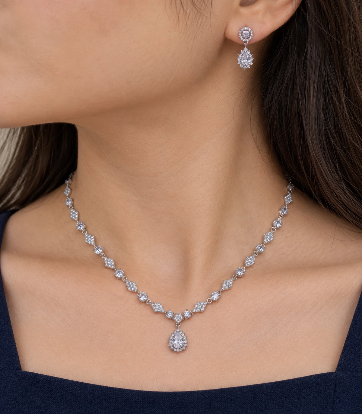 Close view of clear teardrop earring and silver-tone necklace worn naturally
