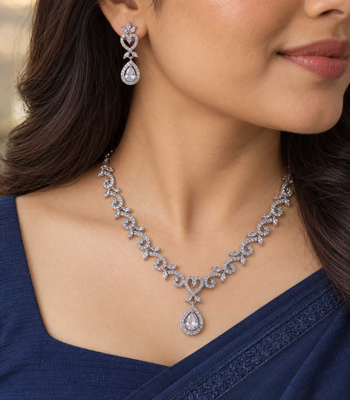Worn close view of clear heart and teardrop earring with the matching scrolling necklace