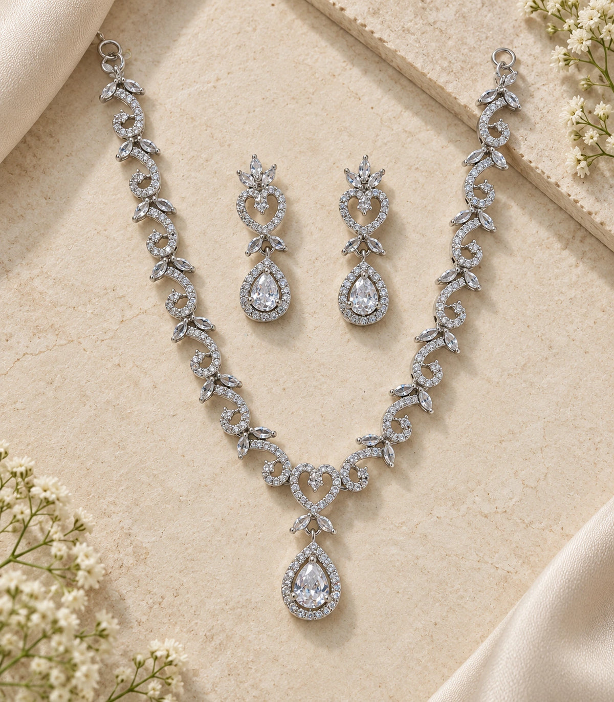 Complete silver-tone clear necklace and both matching earrings arranged on a neutral textured surface