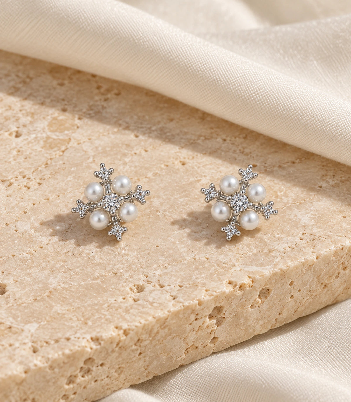 JIMIKI silver crystal pearl snowflake stud earrings, matching pair on textured stone #color_silver