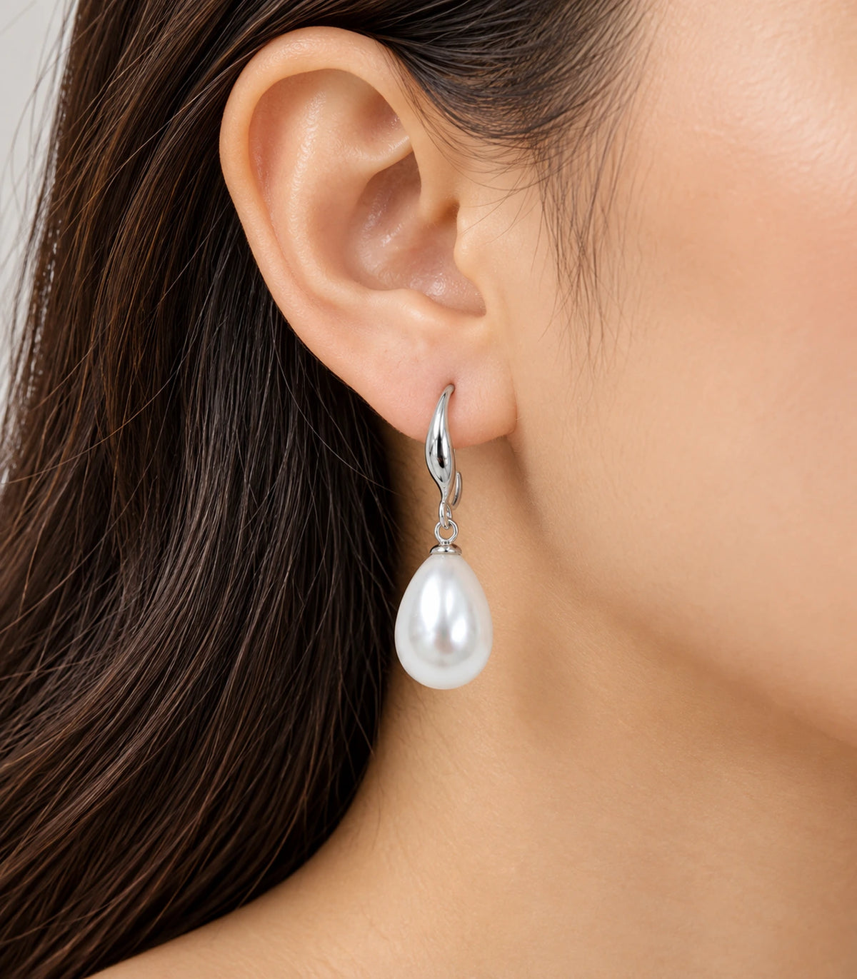 Editorial ear view of a silver-tone curved leaf earring with a white teardrop pearl-style drop