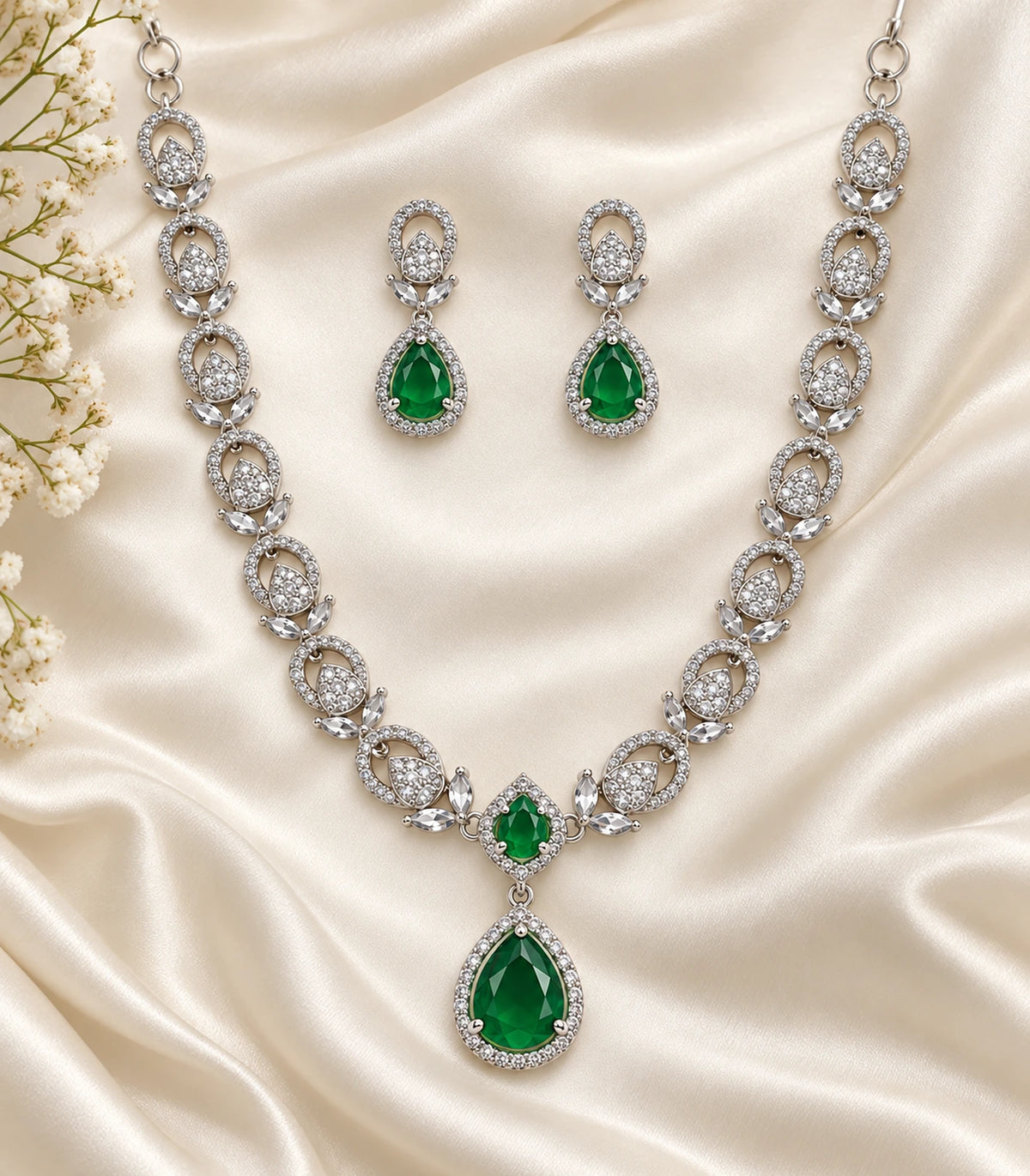 Silver-tone green teardrop necklace and matching earring pair arranged on ivory fabric