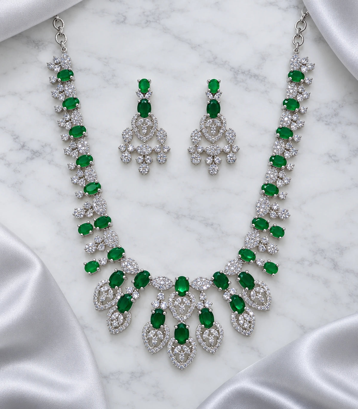 Emerald-green necklace and matching pair of earrings arranged on marble with pale fabric