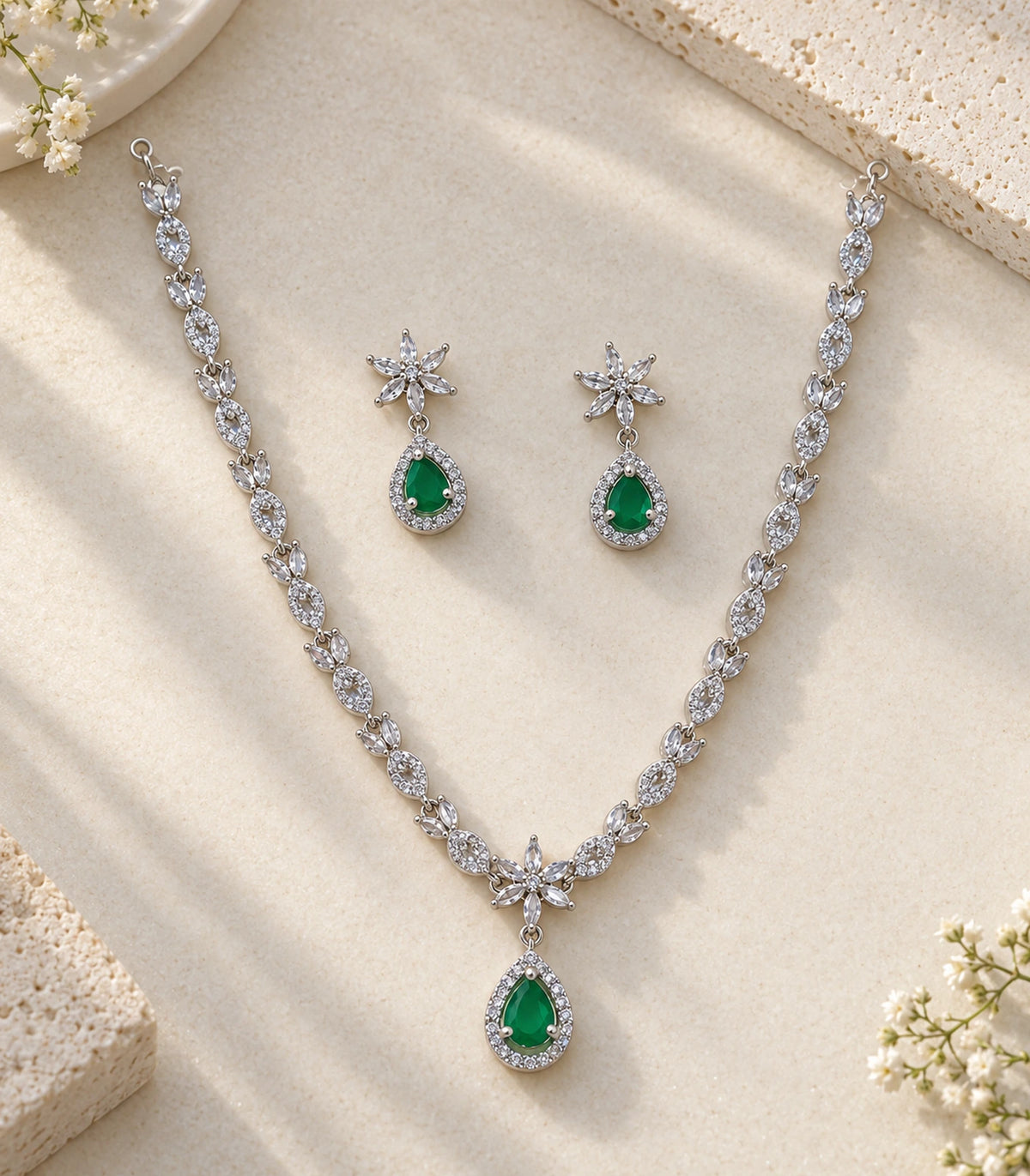 Complete silver-tone necklace and matching emerald-green teardrop earrings arranged on a light textured surface