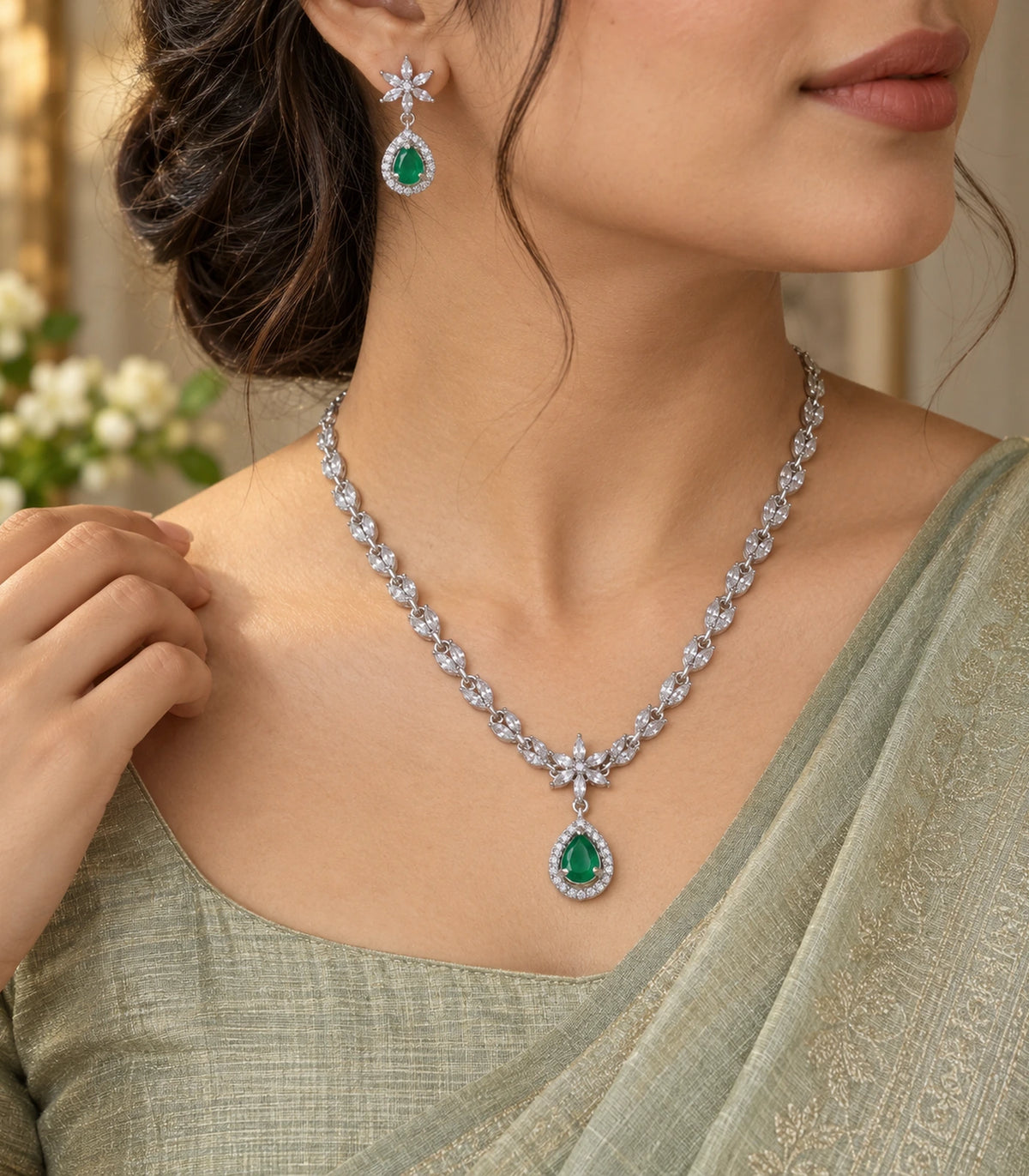 Silver-tone floral necklace and emerald-green drop earring worn in warm editorial light