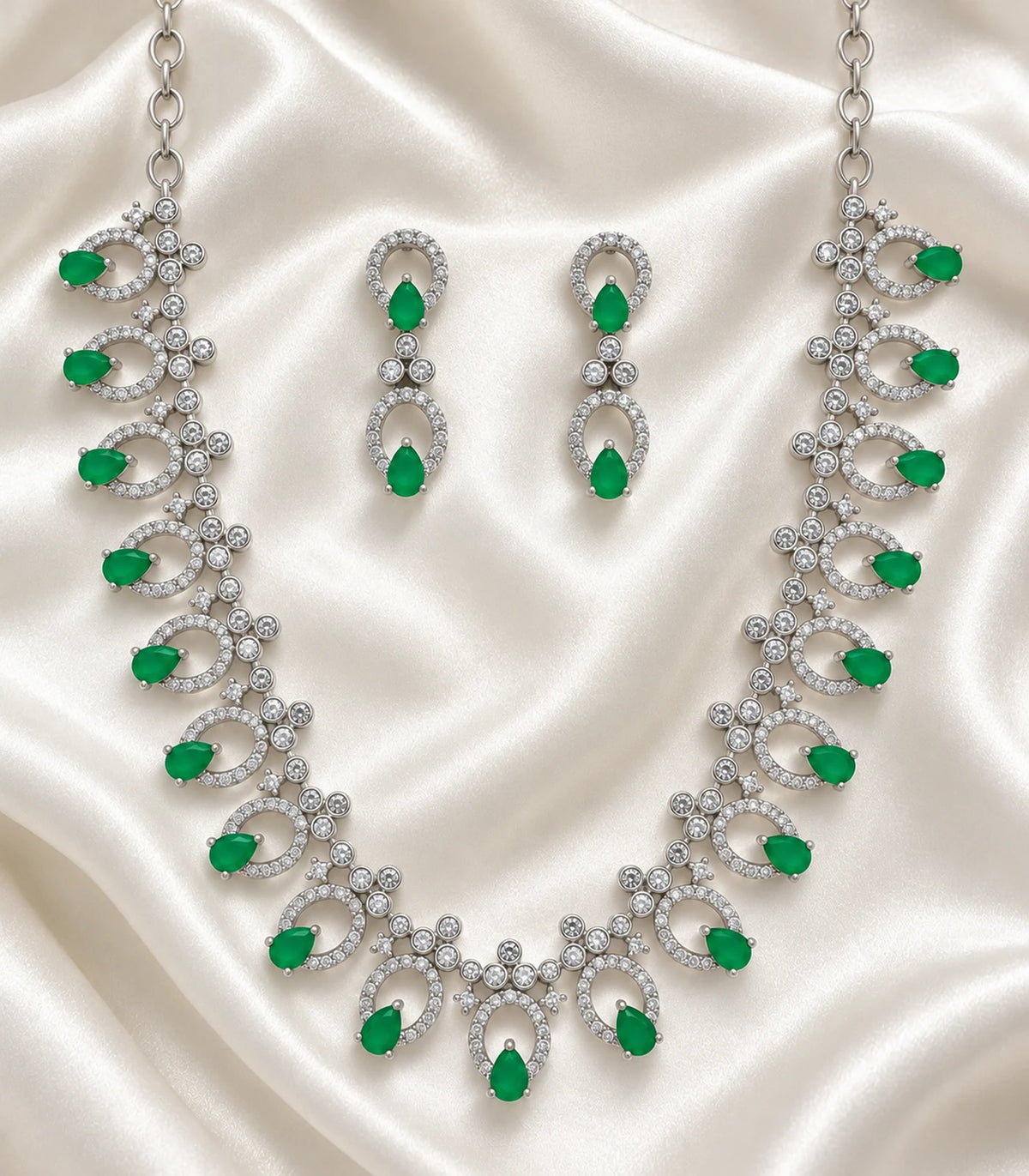 Silver-tone emerald-green necklace and matching pair of earrings arranged on satin