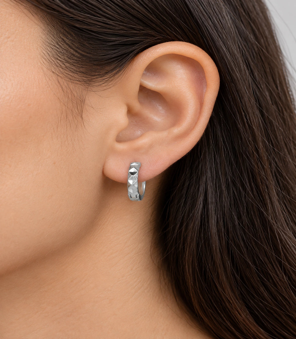 JIMIKI silver faceted diamond pattern huggie earrings, worn on the ear #color_silver