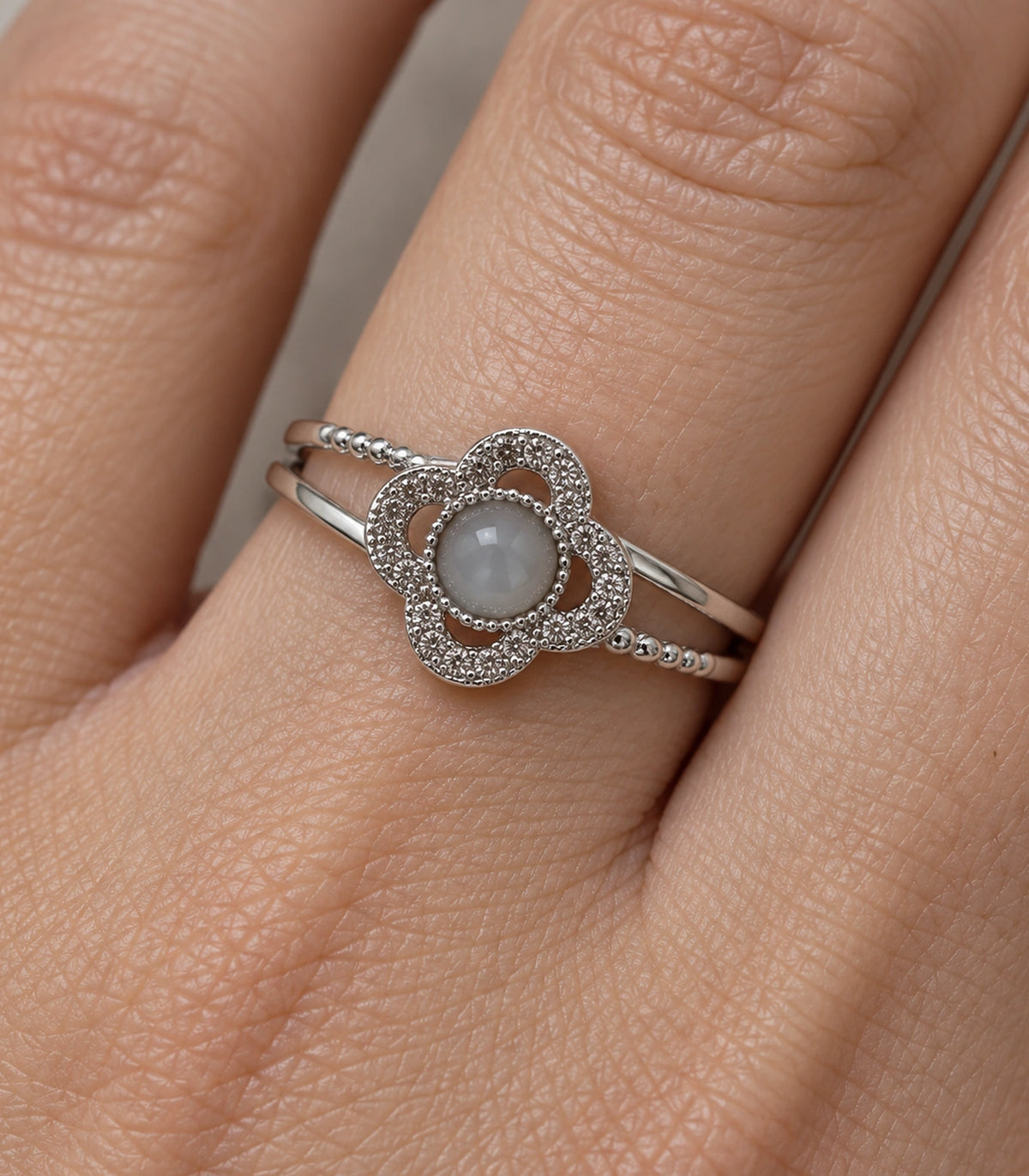 Close view of grey cabochon, four-lobed halo and split band on a finger