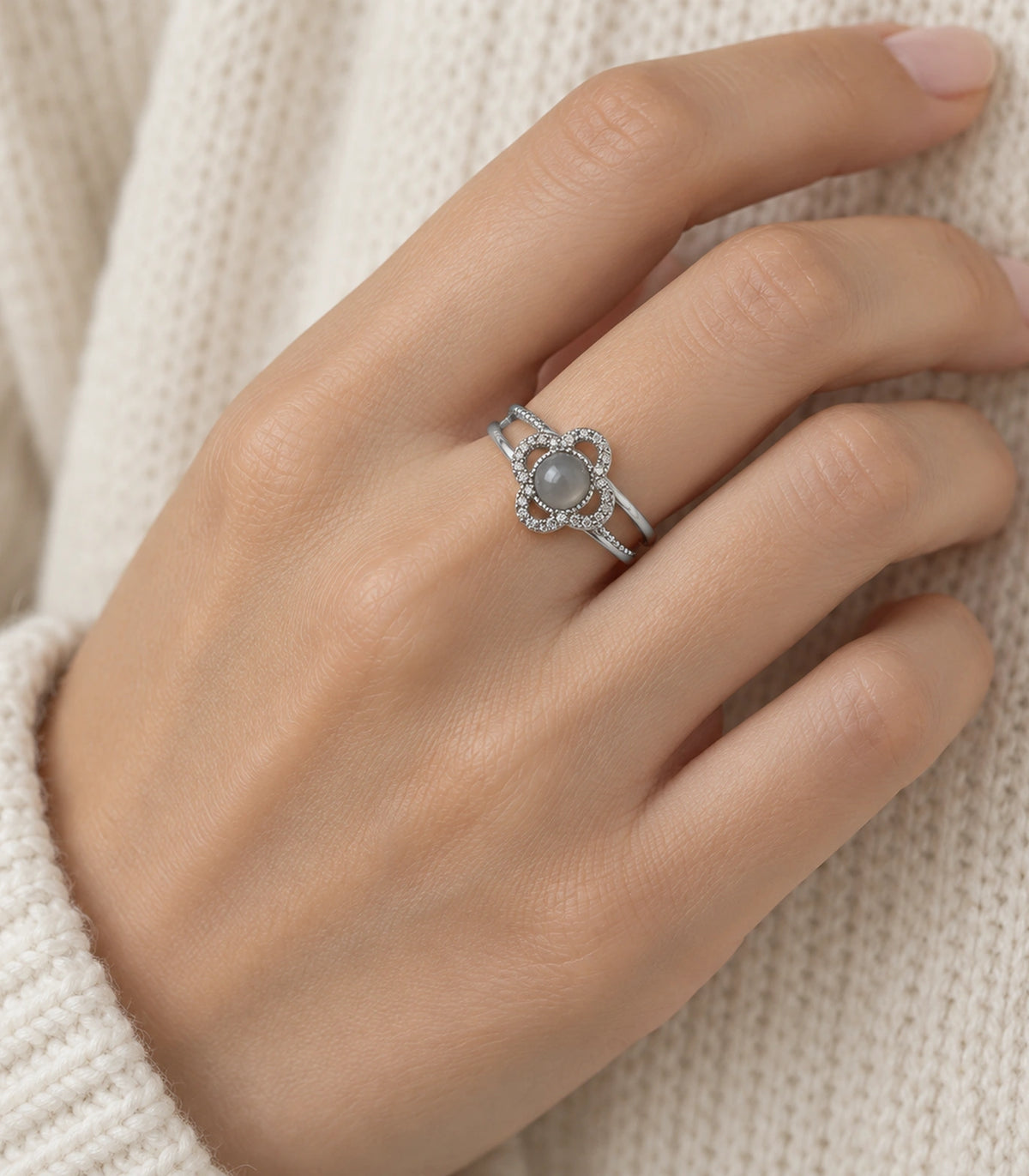 Silver grey clover halo ring worn on a hand against cream knitwear