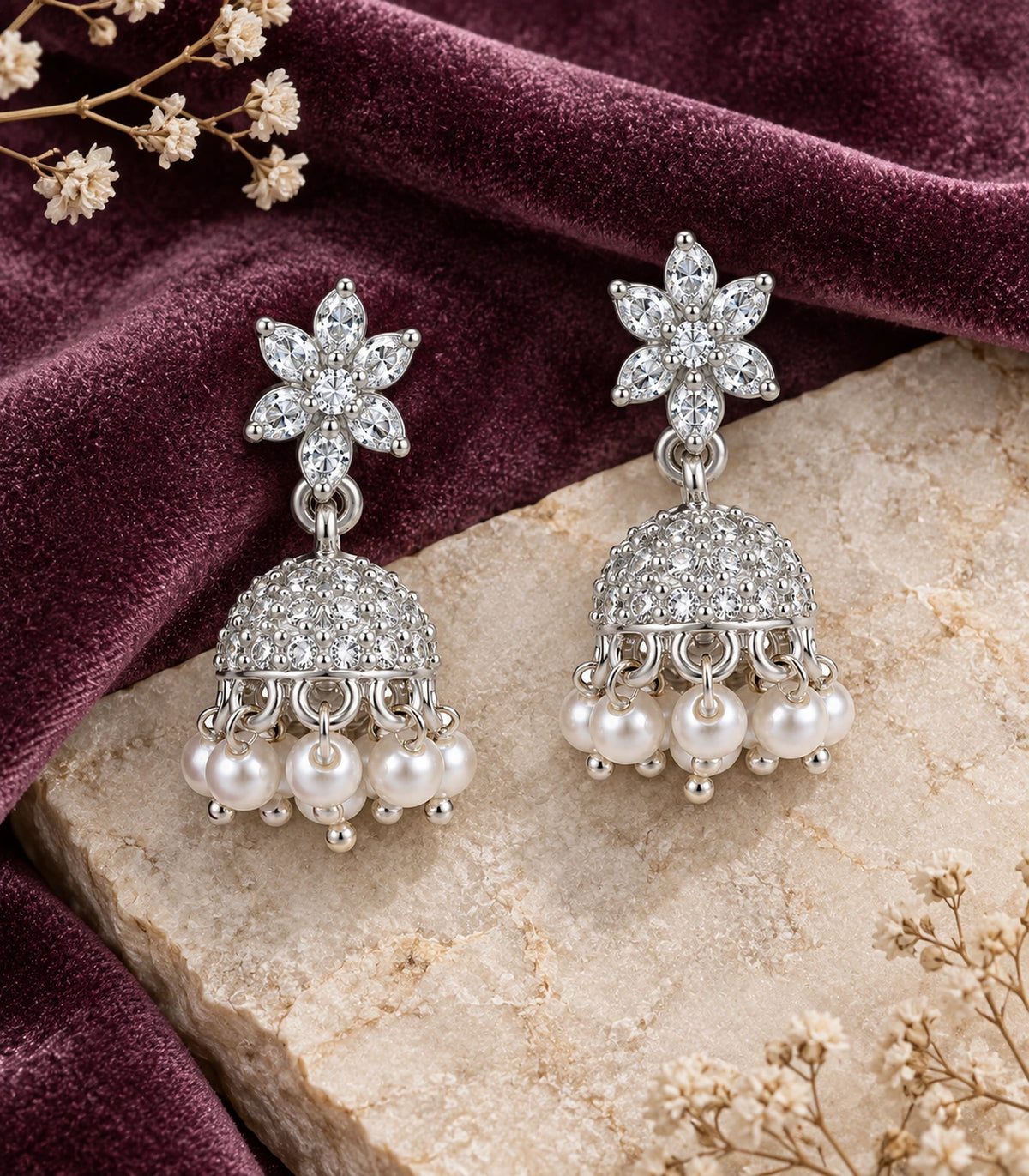 JIMIKI Silver Leaf Flower Crystal Jhumka Earrings - Matching pair on pale stone beside plum fabric #color_silver