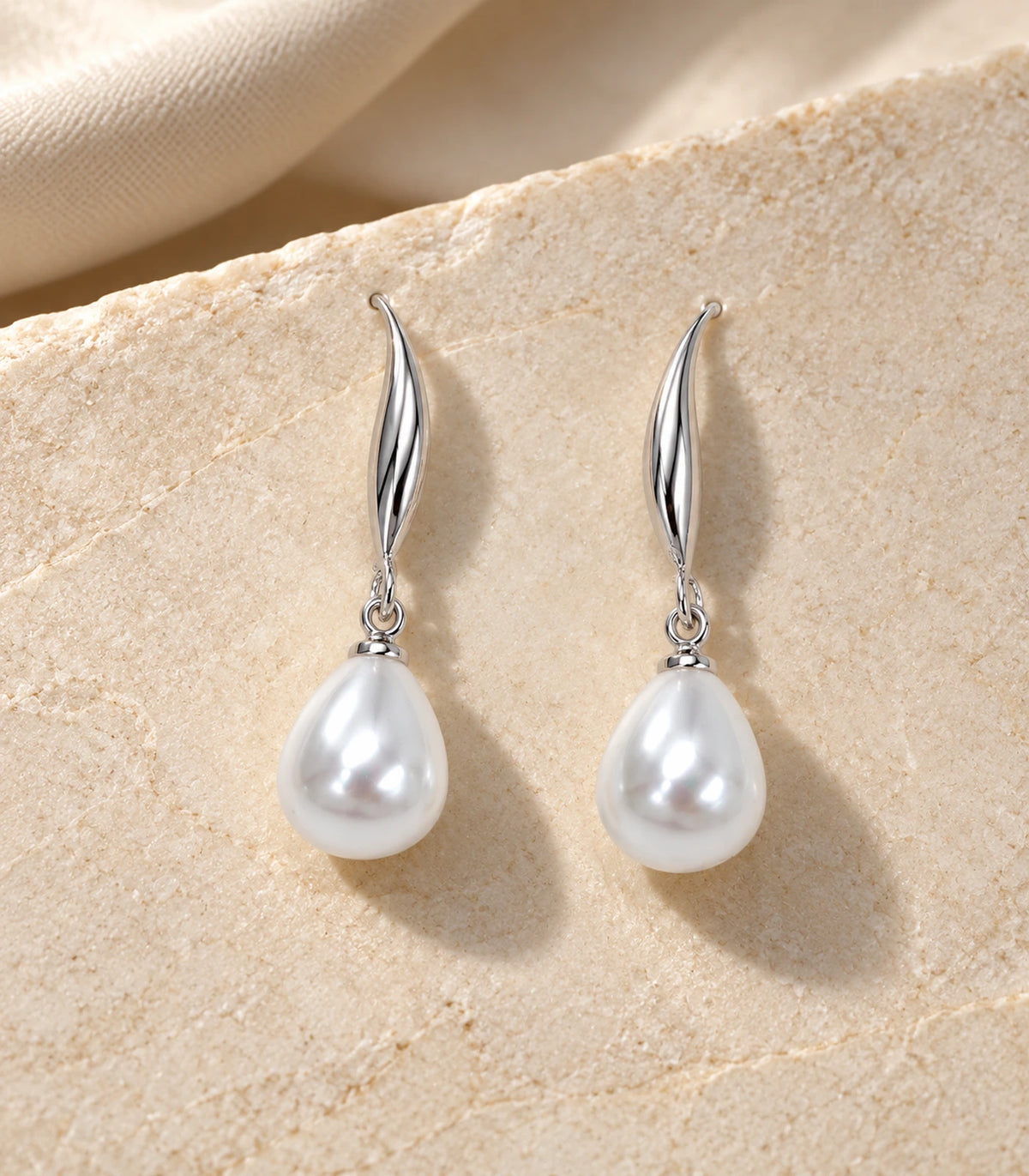 Matching pair of silver-tone leaf earrings with white pearl-style drops arranged on cream stone