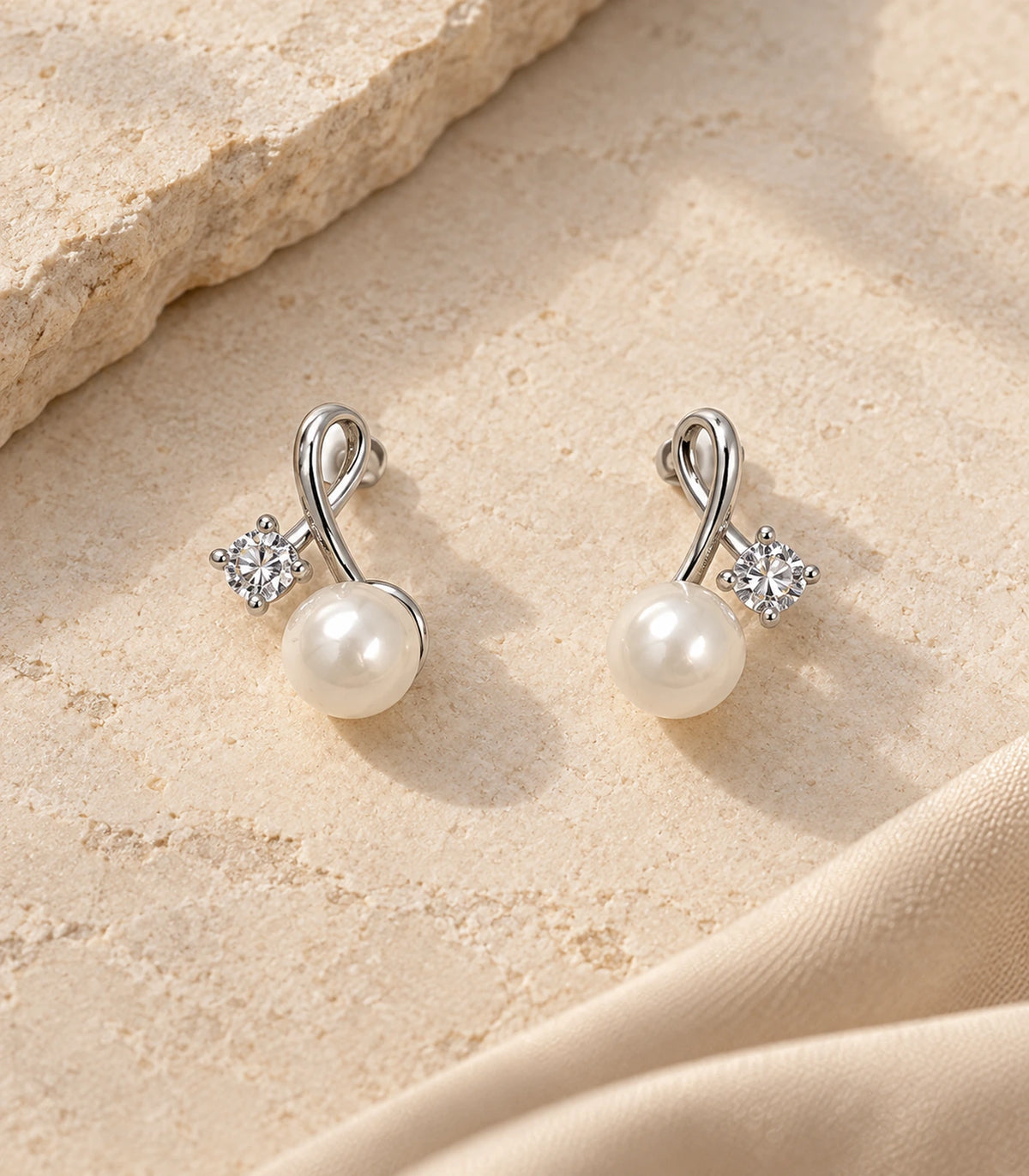 Matching pair of silver-tone loop crystal and pearl-style earrings arranged on a neutral stone surface