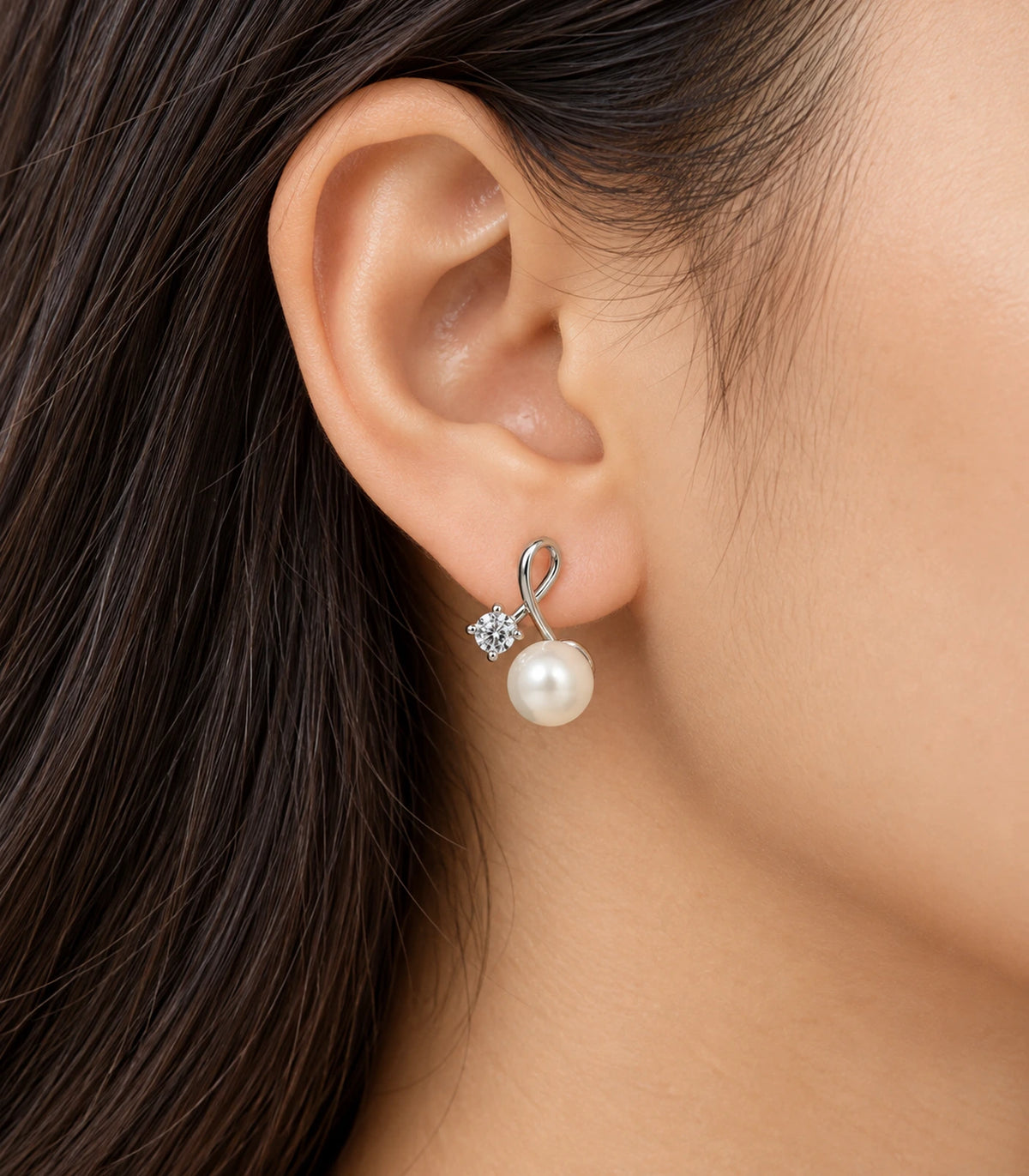 Silver-tone loop earring worn on one ear, showing the clear round accent beside the white pearl-style drop