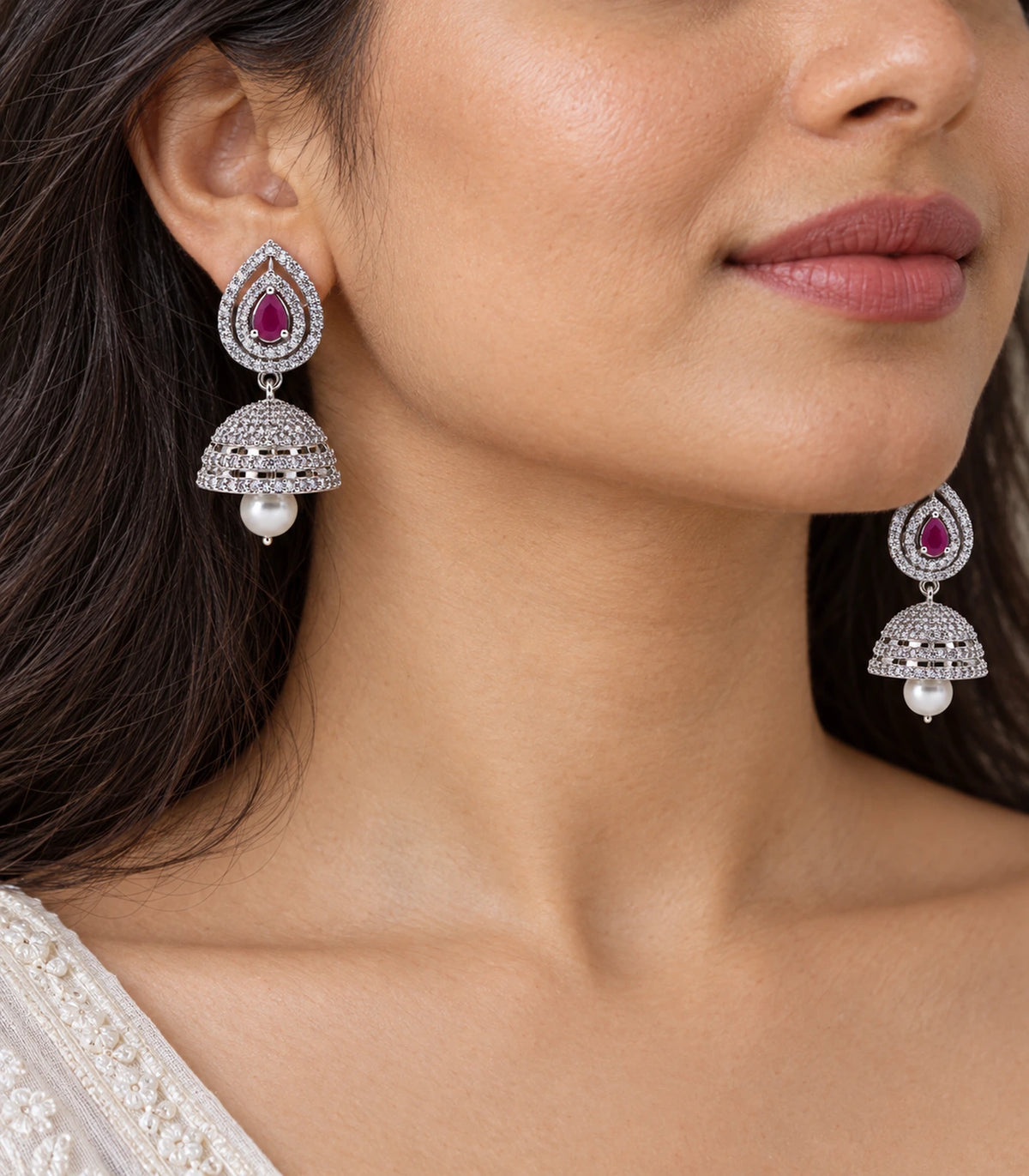 Close view of magenta double halo jhumka earrings with clear detailing and white drops worn on a model