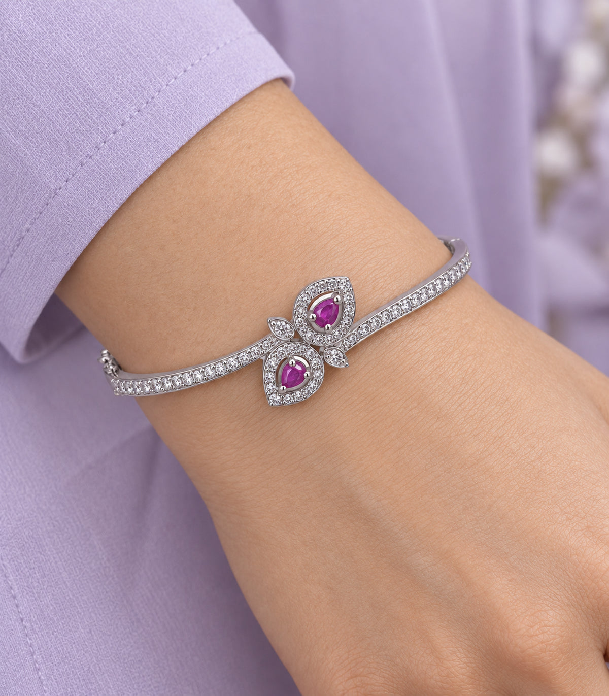 Close view of the bangle's two magenta teardrops, clear leaf halos and small leaves worn beside a lavender sleeve