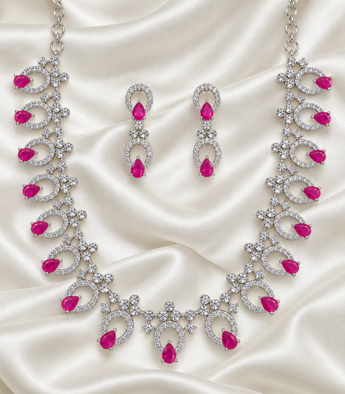 Silver-tone magenta teardrop necklace and matching earring pair arranged on fabric