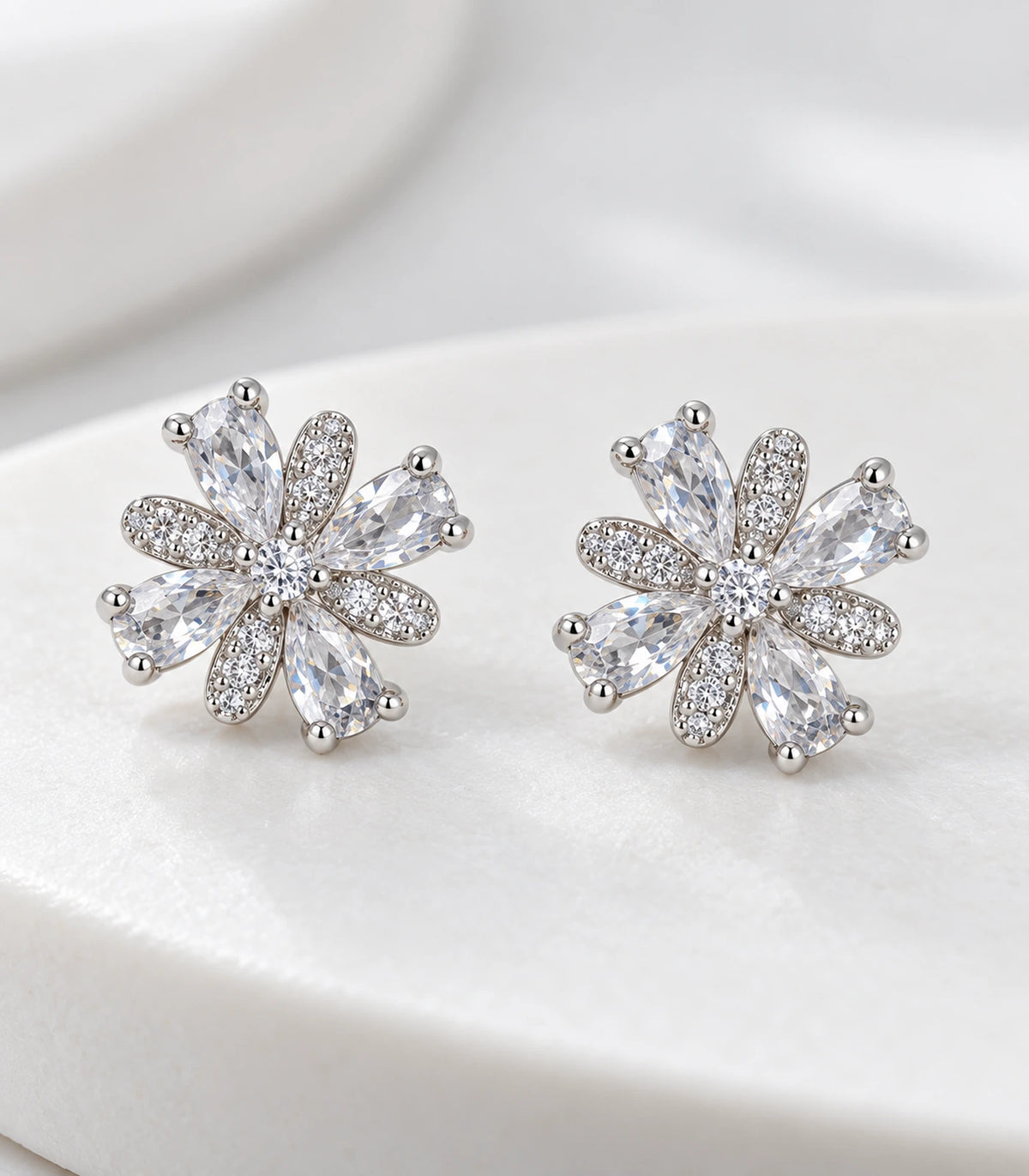 Close view of the matching silver-tone floral stud earring pair on pale fabric