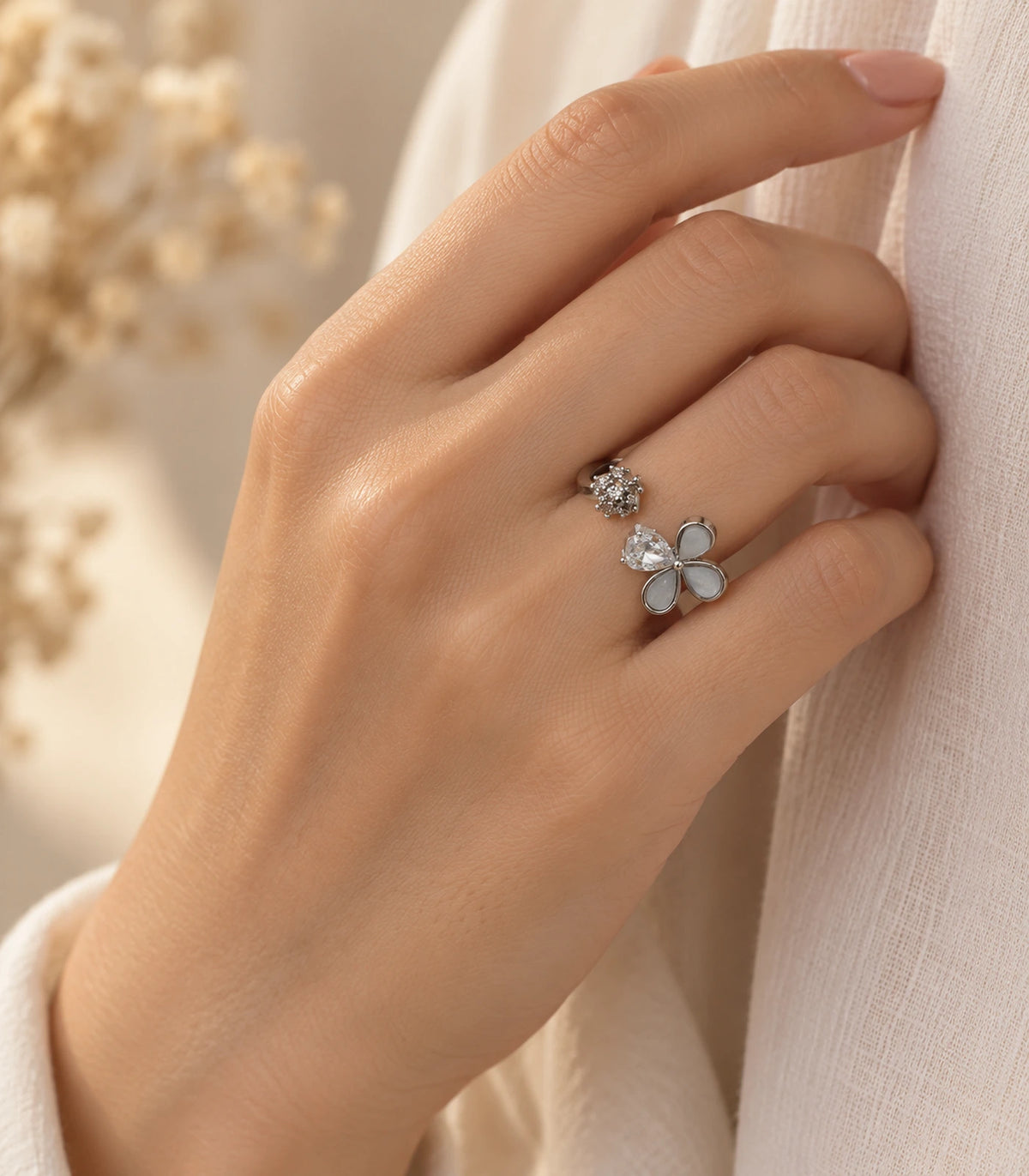 Silver-tone flower and crystal open ring worn in a distinct hand pose against light fabric