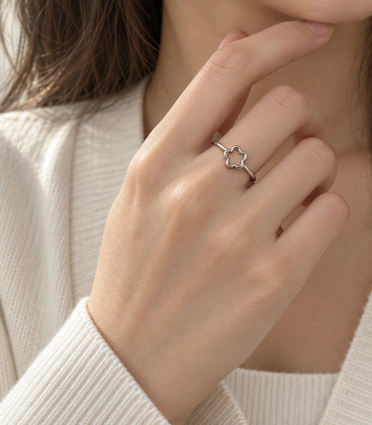 Silver-tone five-petal flower ring worn on a hand near the chin with a cream knit outfit