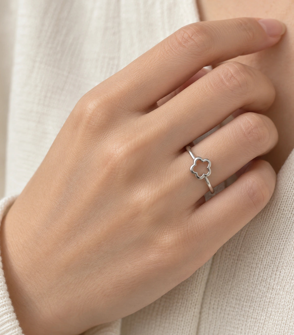 Silver-tone hollow five-petal flower ring worn naturally on a hand with a cream knit sleeve