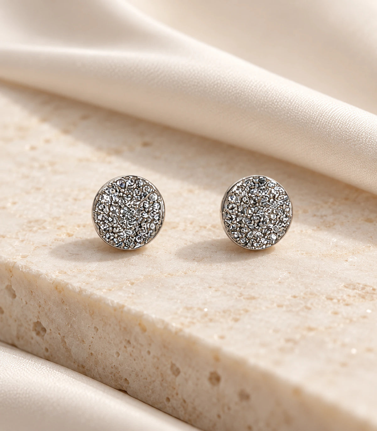 Matching silver-tone pavé round disc stud earrings styled on a stone surface