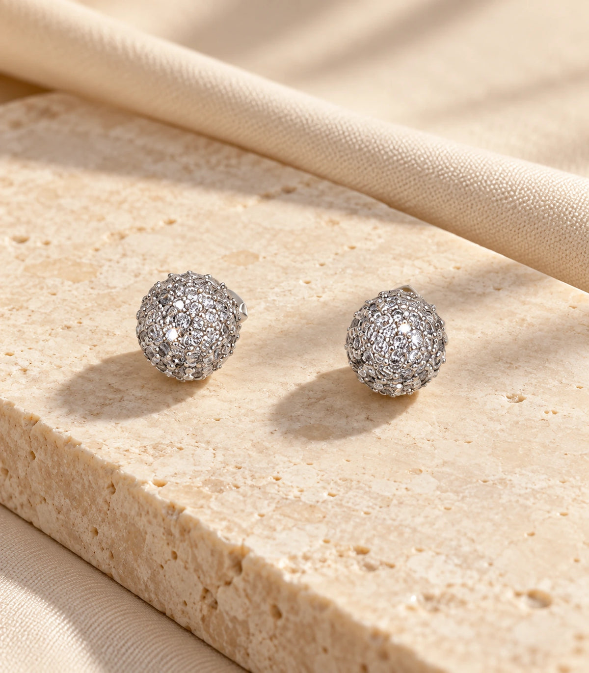 Pair of silver-tone pavé sphere stud earrings in a stone flatlay