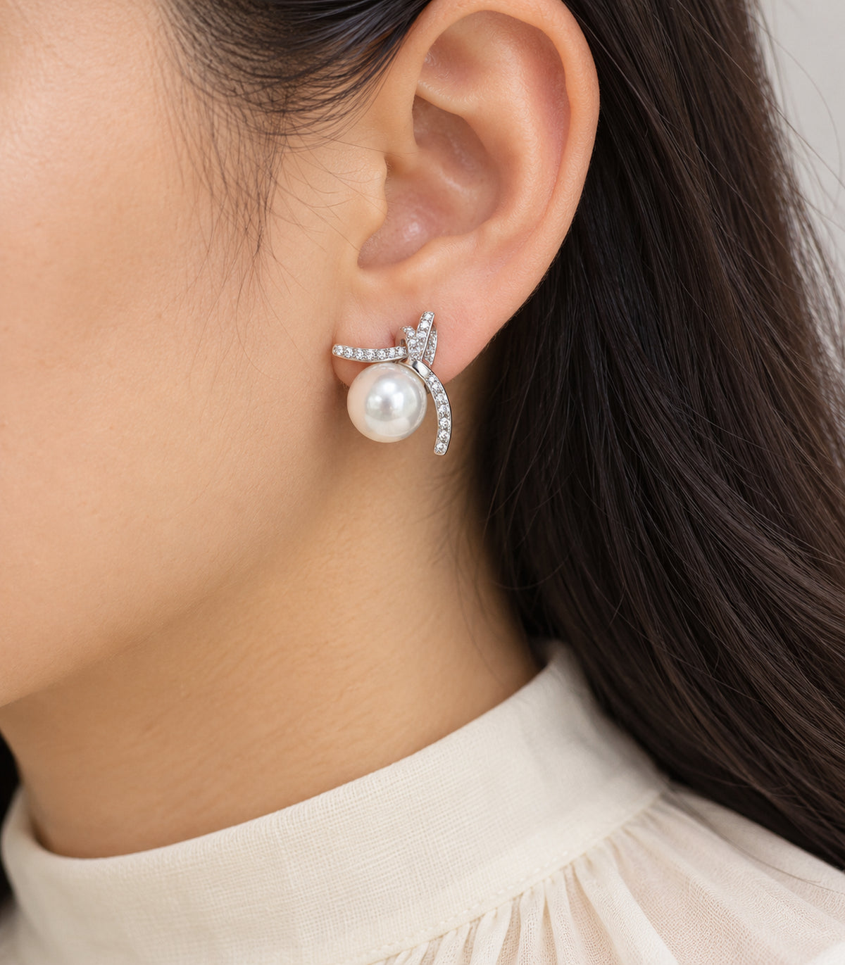Close view of the pearl-look bead and three pavé arms of a silver-tone stud earring worn on one ear