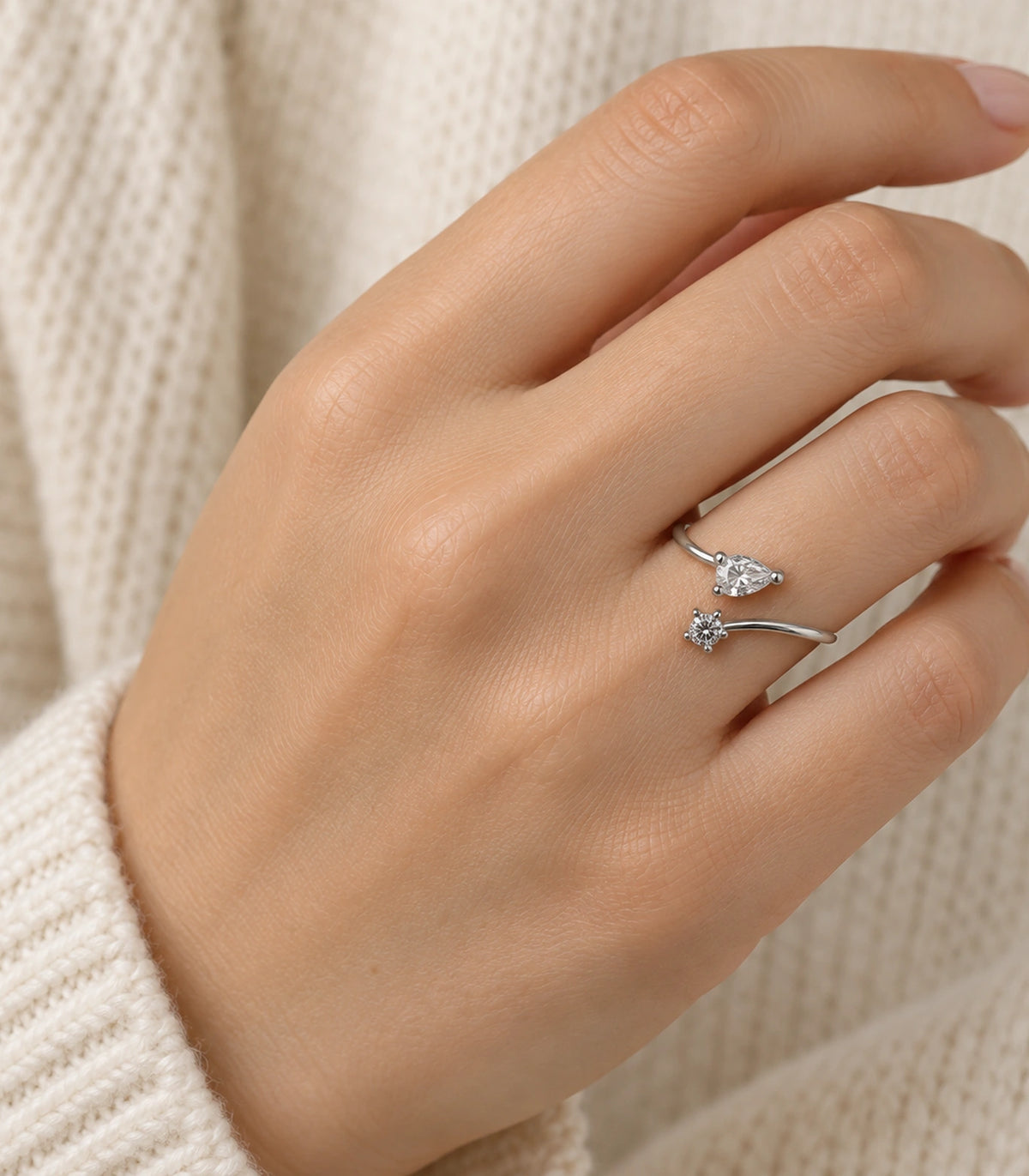 Silver-tone two-stone bypass ring worn naturally on a hand with a cream knit sleeve
