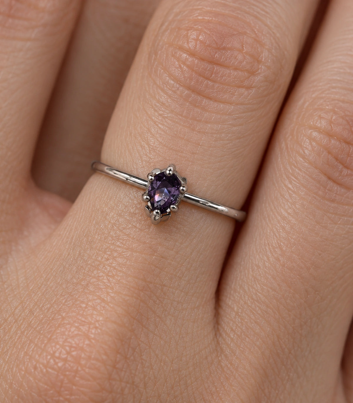 Closeup of the purple oval stone and six-prong silver-tone ring setting worn on a finger
