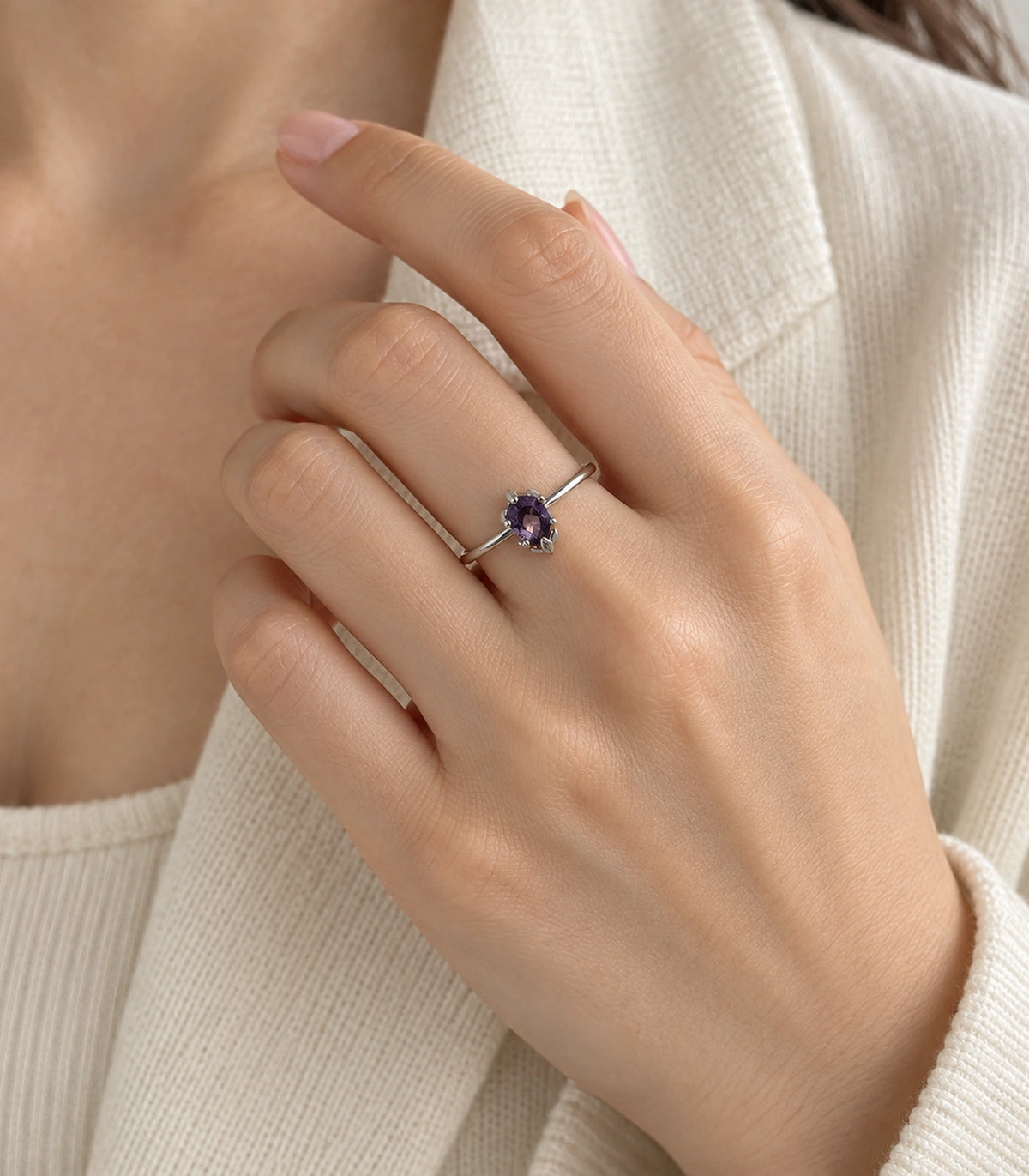Purple oval solitaire ring worn in a distinct hand-to-collar pose with a white garment
