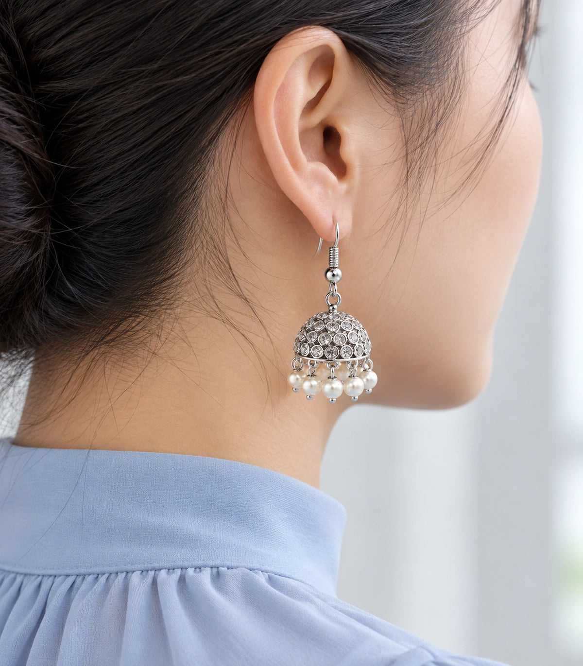Editorial view of a silver-tone crystal-style pearl-effect jhumka with hair tied back #color_silver