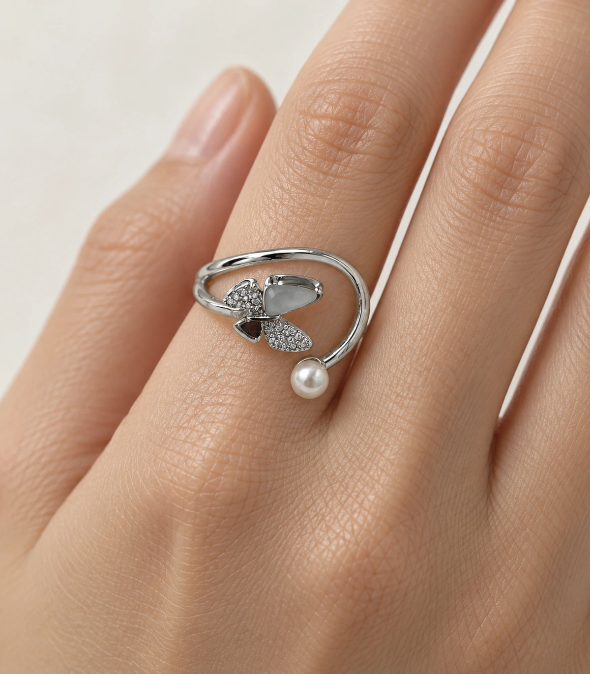 Closeup of silver swirl open ring showing pearl-like end, pale and dark insets and crystal-style details