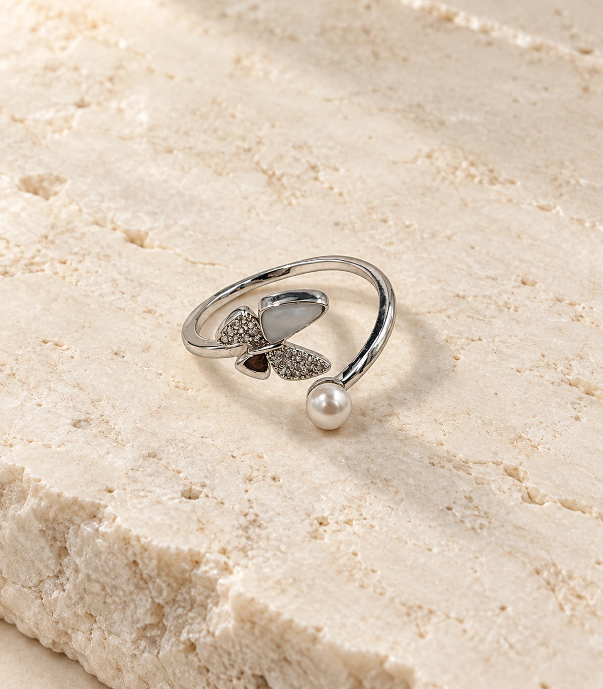 Complete silver swirl pearl crystal open ring on a warm stone surface