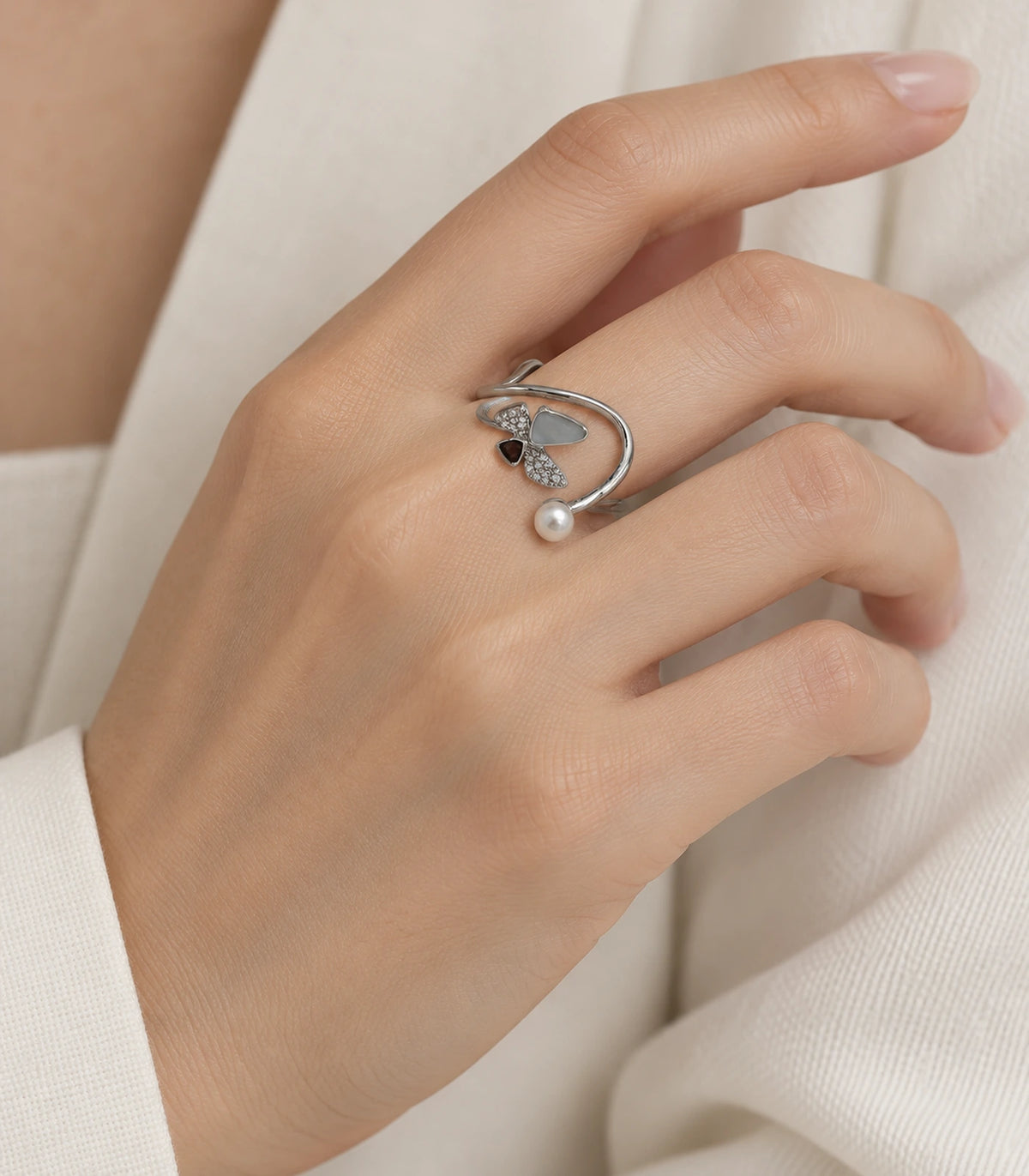 Silver swirl pearl crystal open ring worn naturally on a finger with cream sleeve
